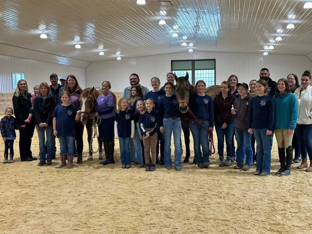 Group of children and adults standing in an indoor equestrian arena with two horses. Free community event. NorthWoods Farm open house  at NorthWoods Farm, Dushore, PA