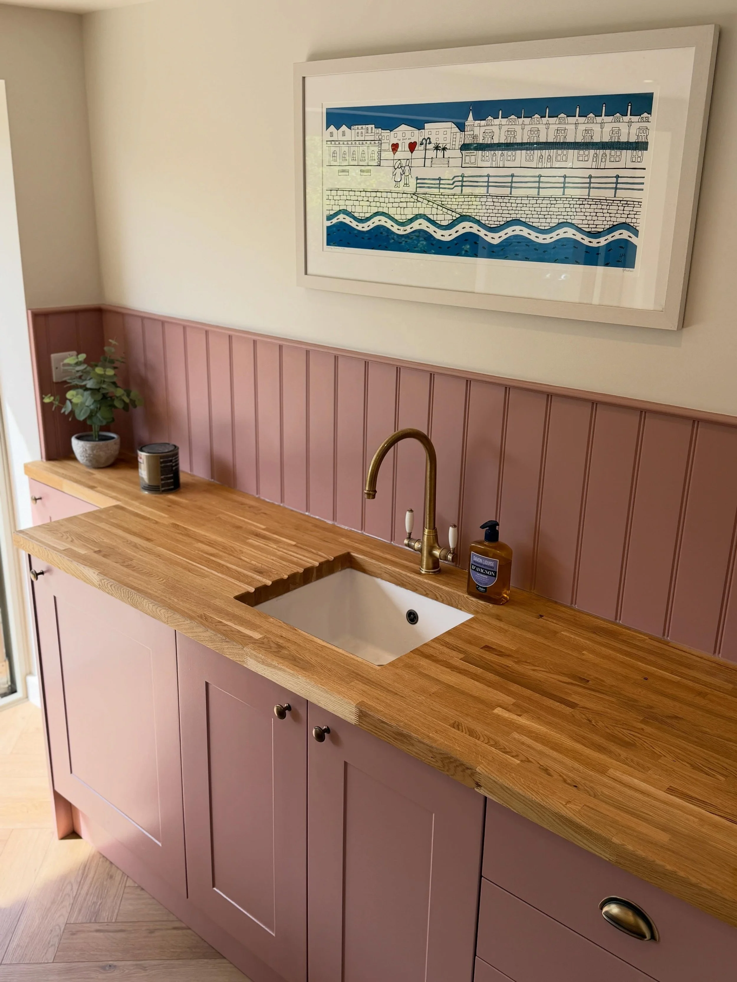 A bespoke kitchenette featuring custom-painted shaker-style cabinetry in a Little Greene paint colour, solid oak worktops, and brushed brass fixtures, designed to complement the garden room perfectly.