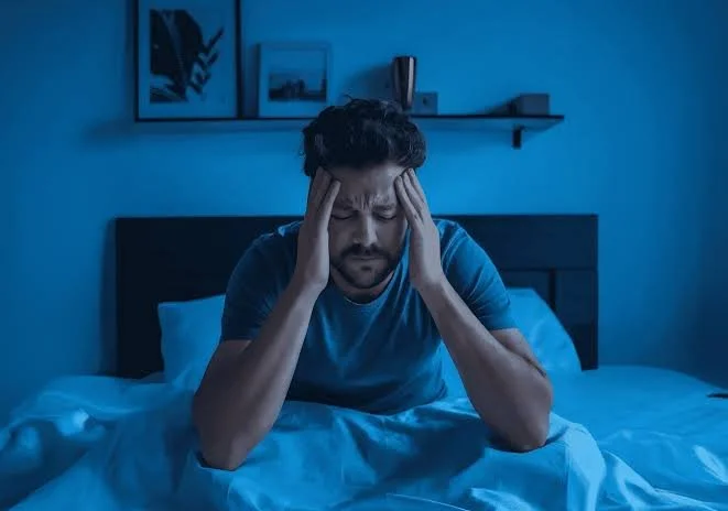Man sitting up in bed at night holding his head, unable to sleep – insomnia