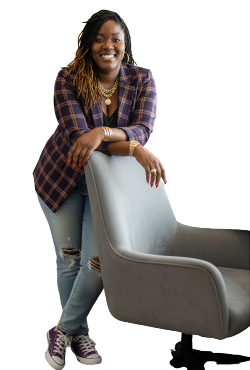 A woman with dreadlocks, wearing a plaid blazer, ripped jeans, and purple sneakers, smiling and leaning on an office chair.