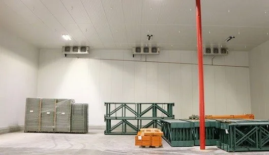 An indoor construction area with metal scaffolding, a red vertical pole, and construction materials stacked on the floor.