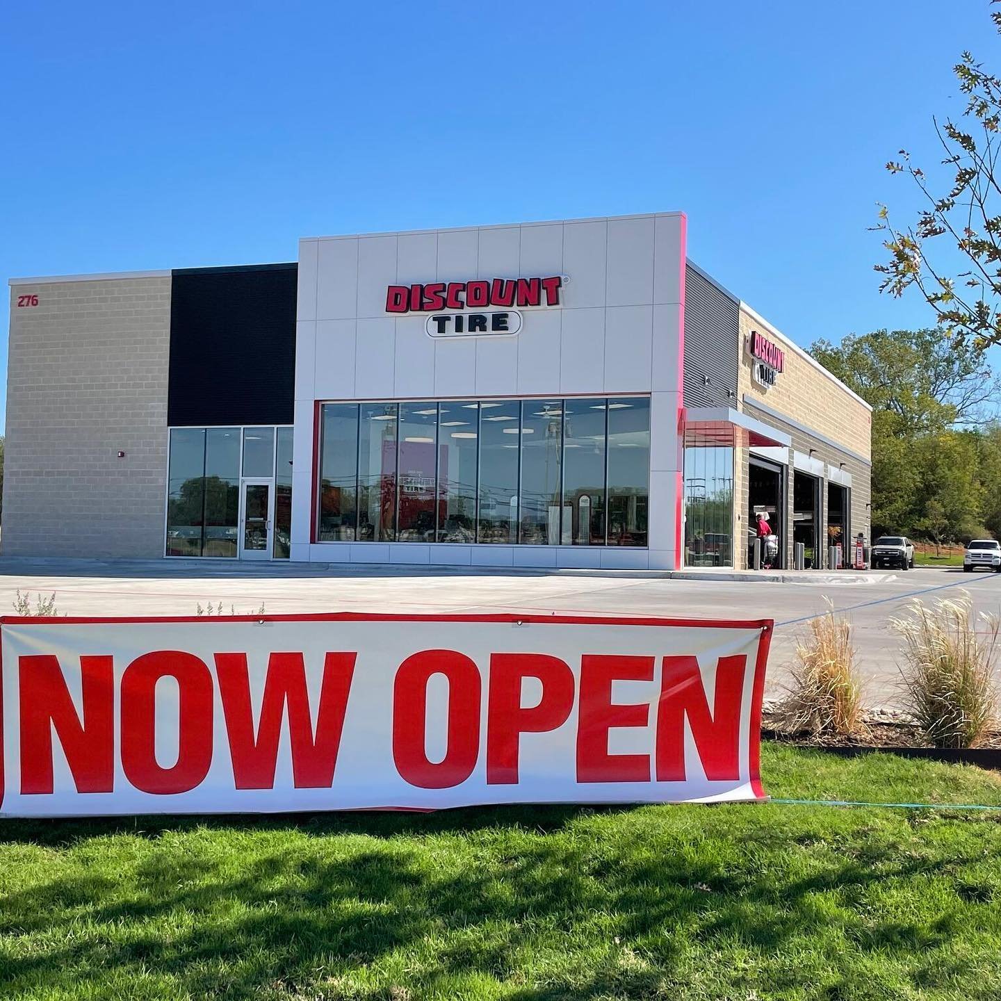 Exterior of a new Discount Tire store with a banner in the lawn that says "Now Open"