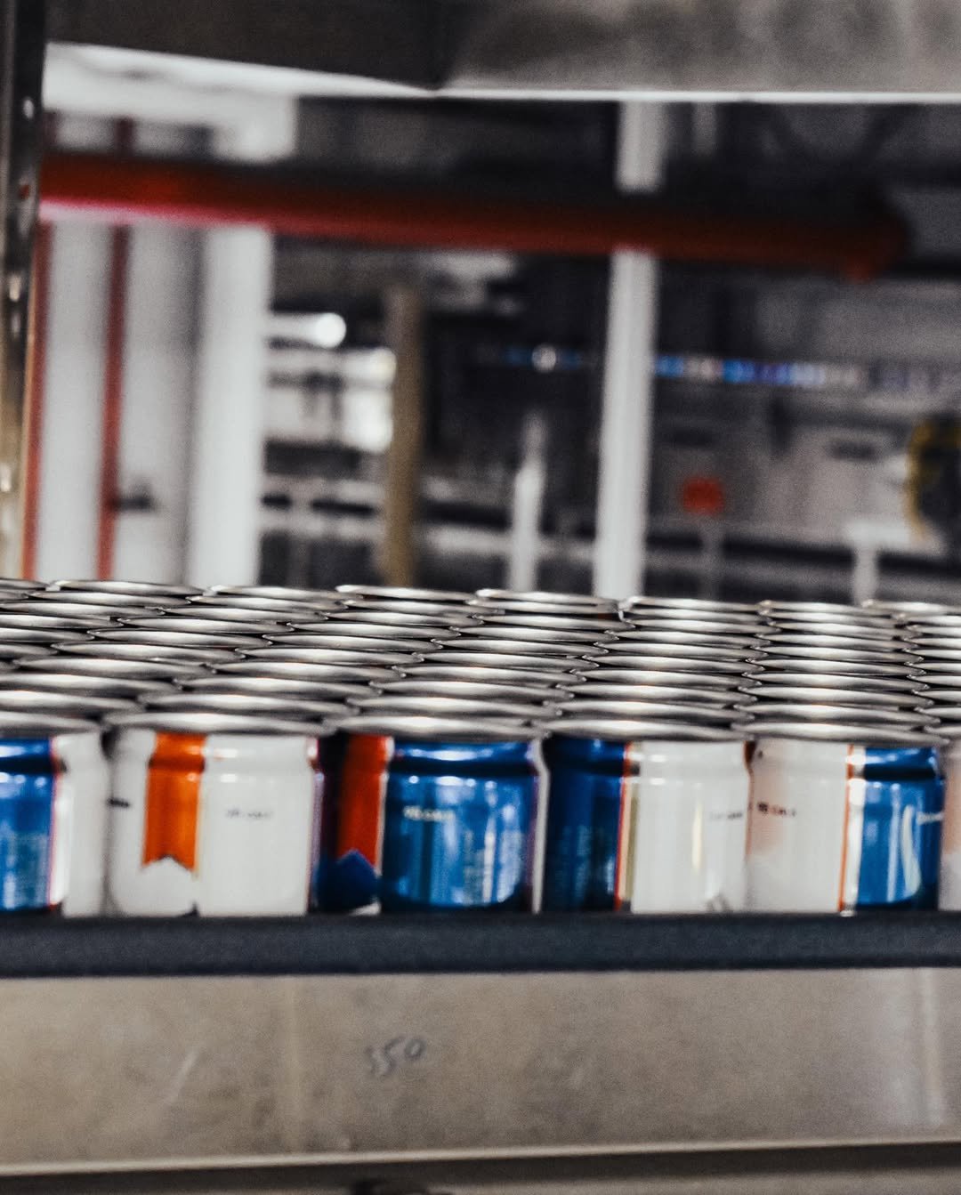 Stack of soda cans arranged in a row on a conveyor belt in an industrial setting.