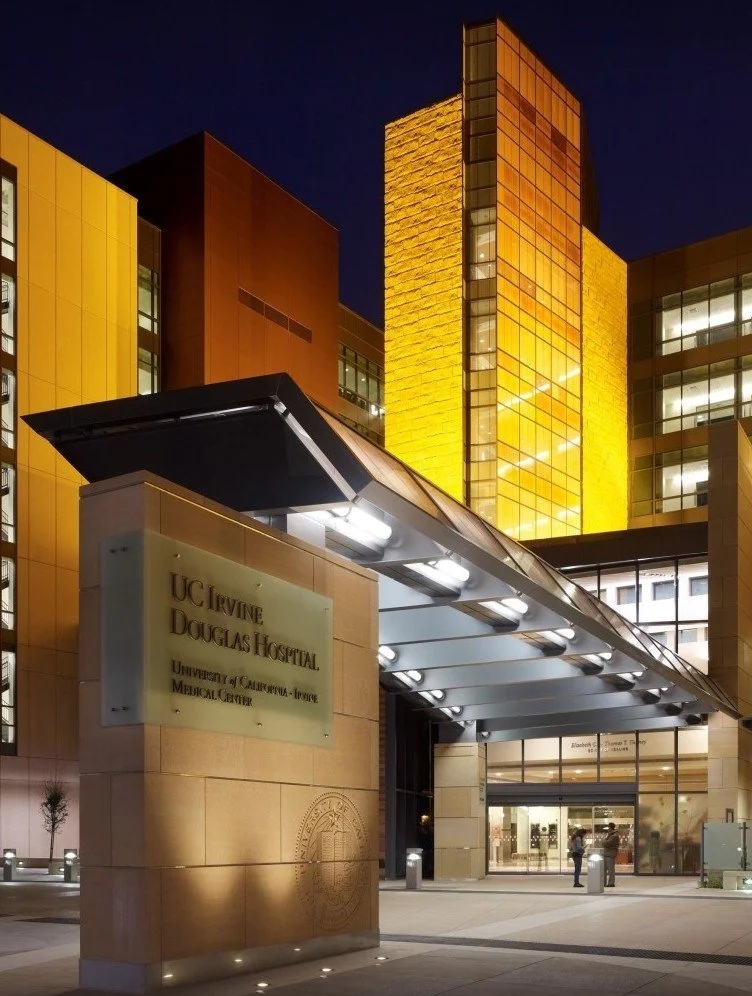 night view of UC Davis' UC Irvine Douglas Hospital at University of California, Irvine Medical Center with illuminated yellow and amber lighting, modern glass facade, and a porte-cochère entrance.