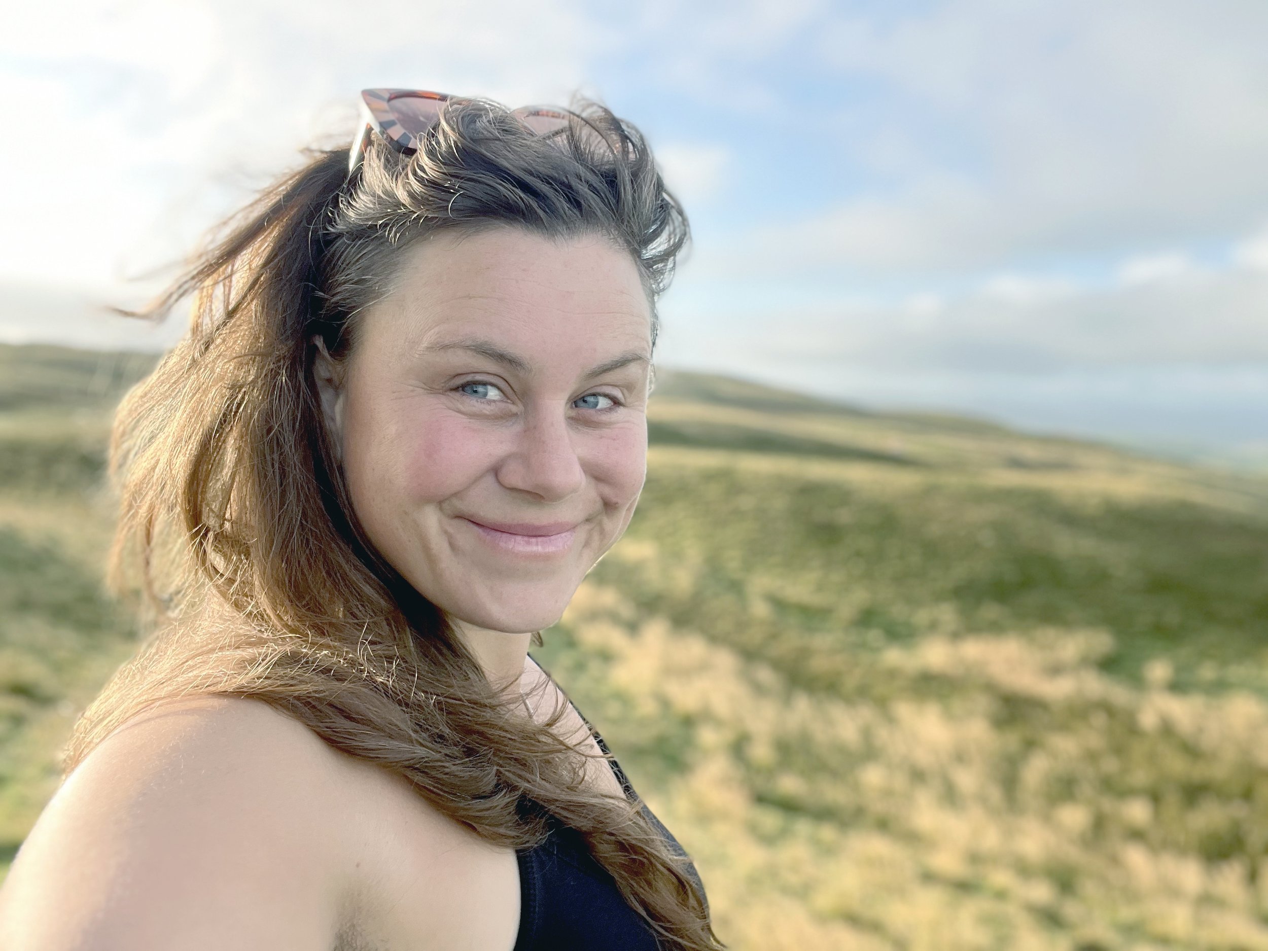 Felix Rowberry in Scotland on a hill, smiling in the sun on a moorland in the early morning light. She's bright, fresh and wears no makeup