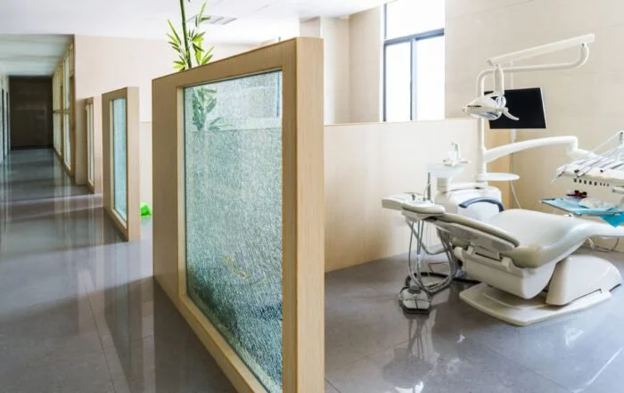 Empty dental clinic with dental chair, equipment, and glass partitions in a modern, bright space.