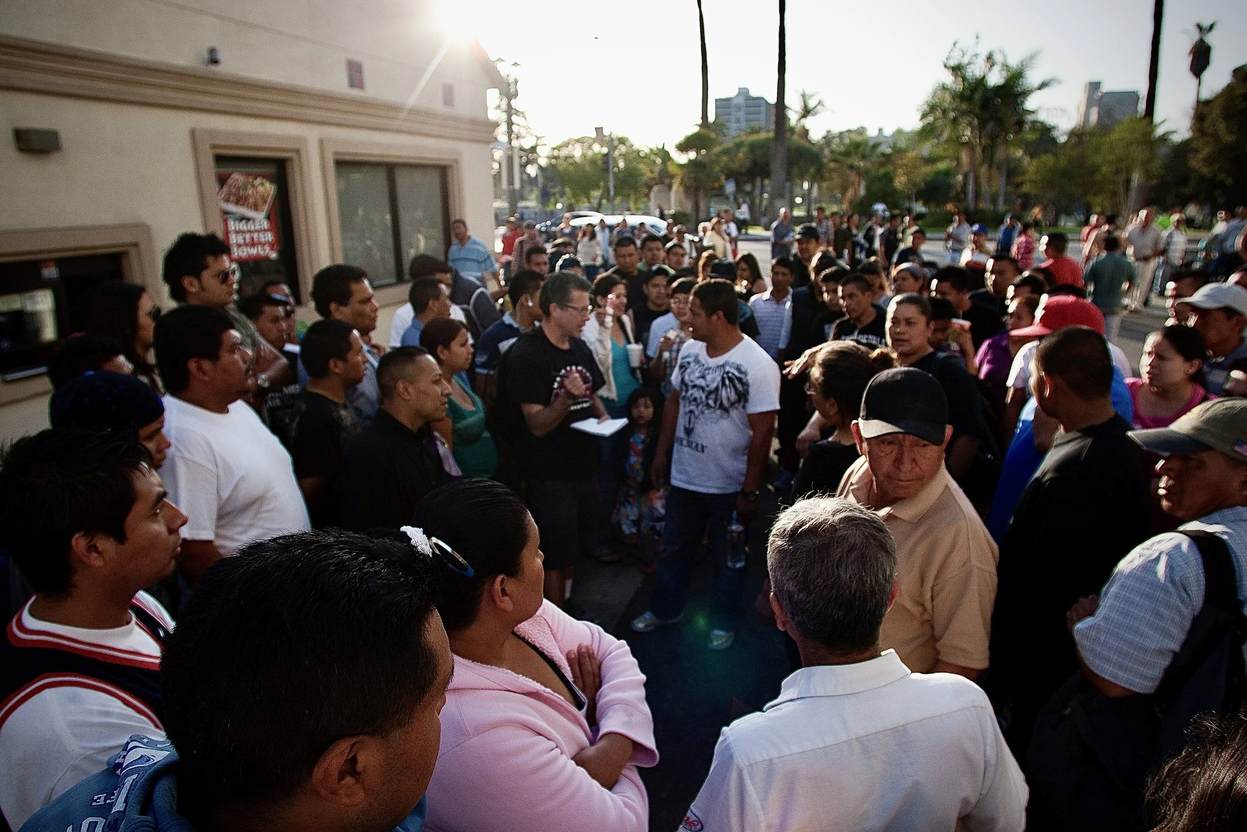 A large crowd of people gathered outside on a sunny day, engaging in conversation.