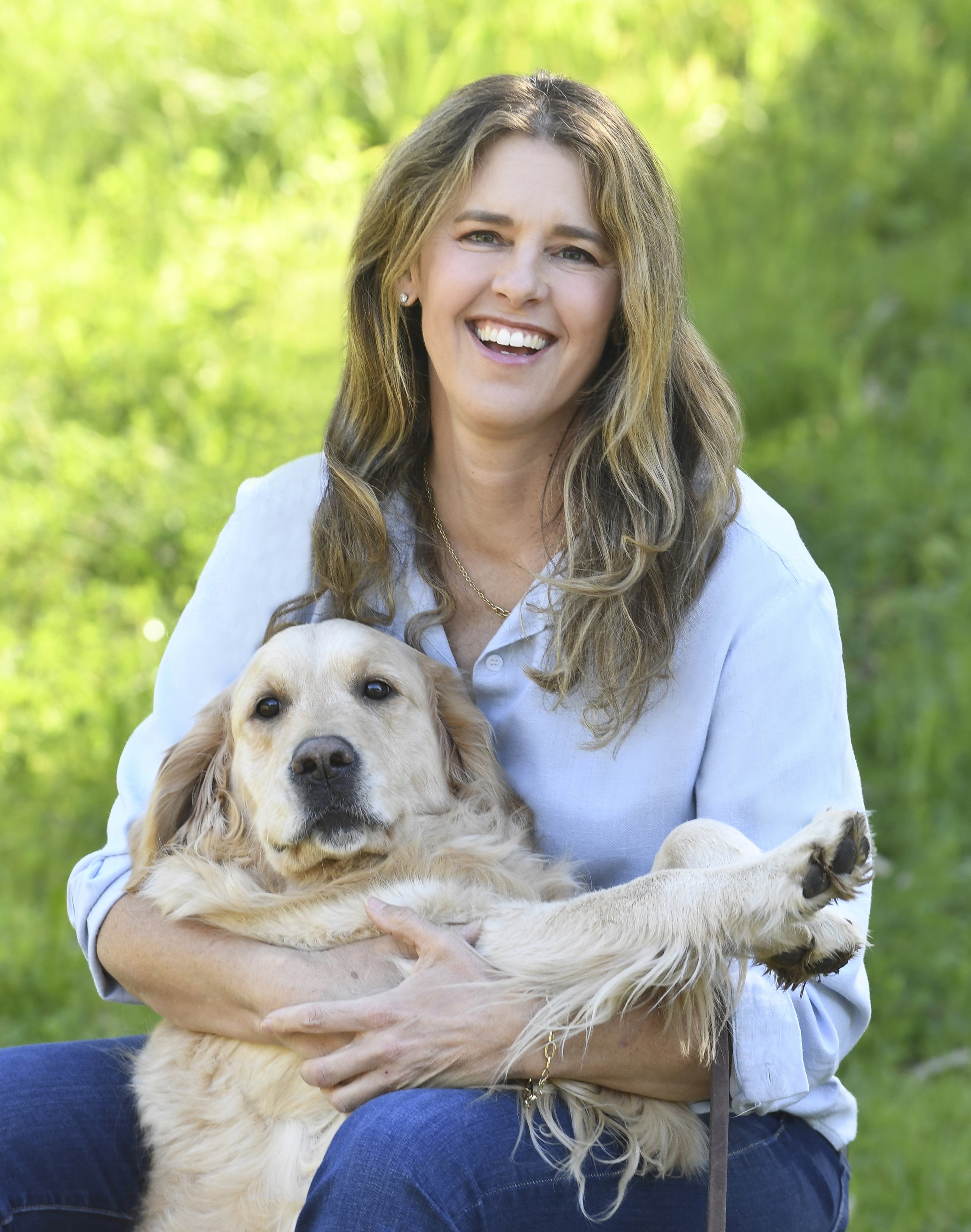 Celebrity dog trainer Jaime Goodrich smiling and holding a golden retriever puppy outdoors with a green blurred background.