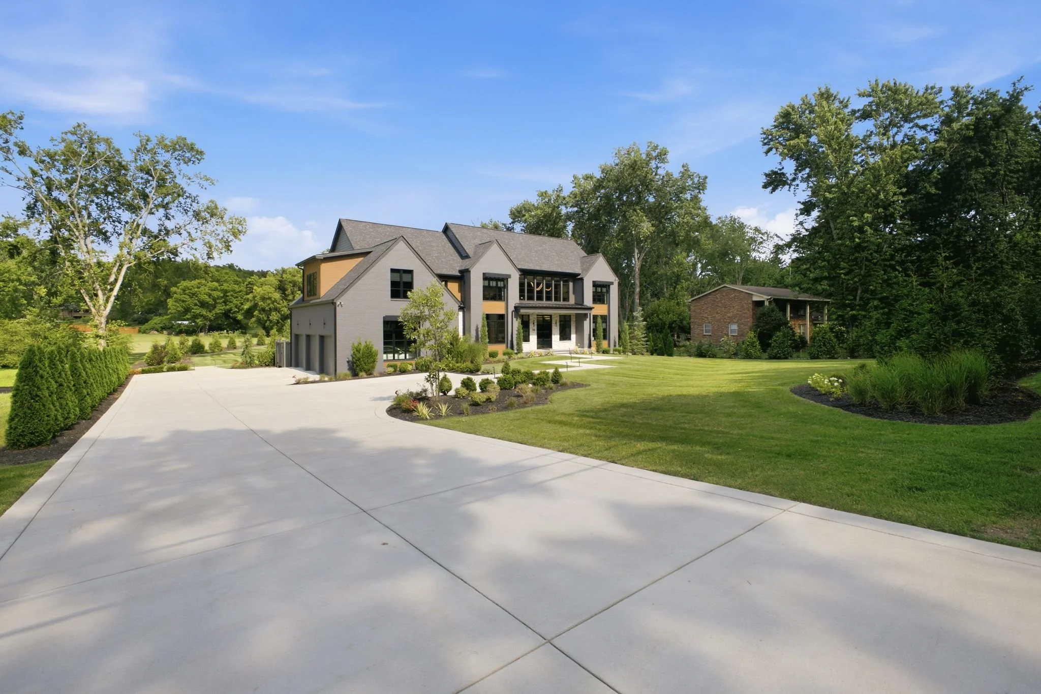 Modern two-story house with a gray brick exterior, black window frames, and a small front porch, surrounded by a well-maintained lawn and trees under a clear blue sky.