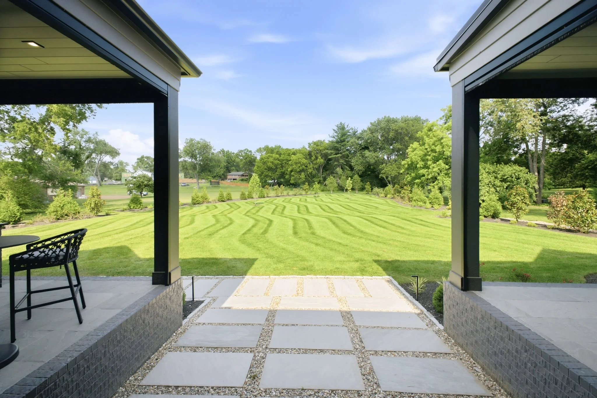 View from a covered patio looking out onto a well-manicured lawn with trees and houses in the distance under a blue sky.