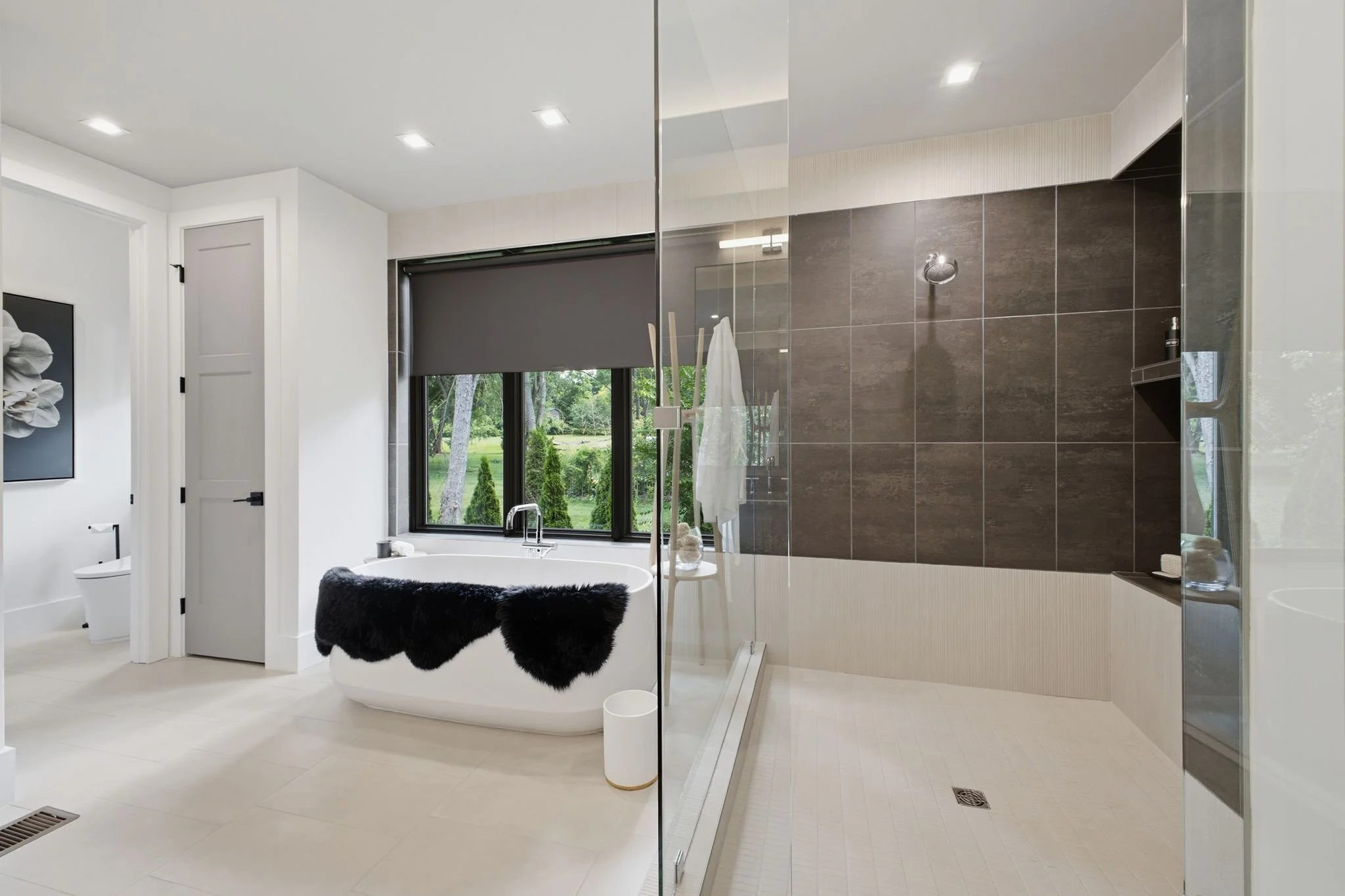 Modern bathroom with a window, bathtub, and shower area, featuring gray and brown tiles and minimalist decor.