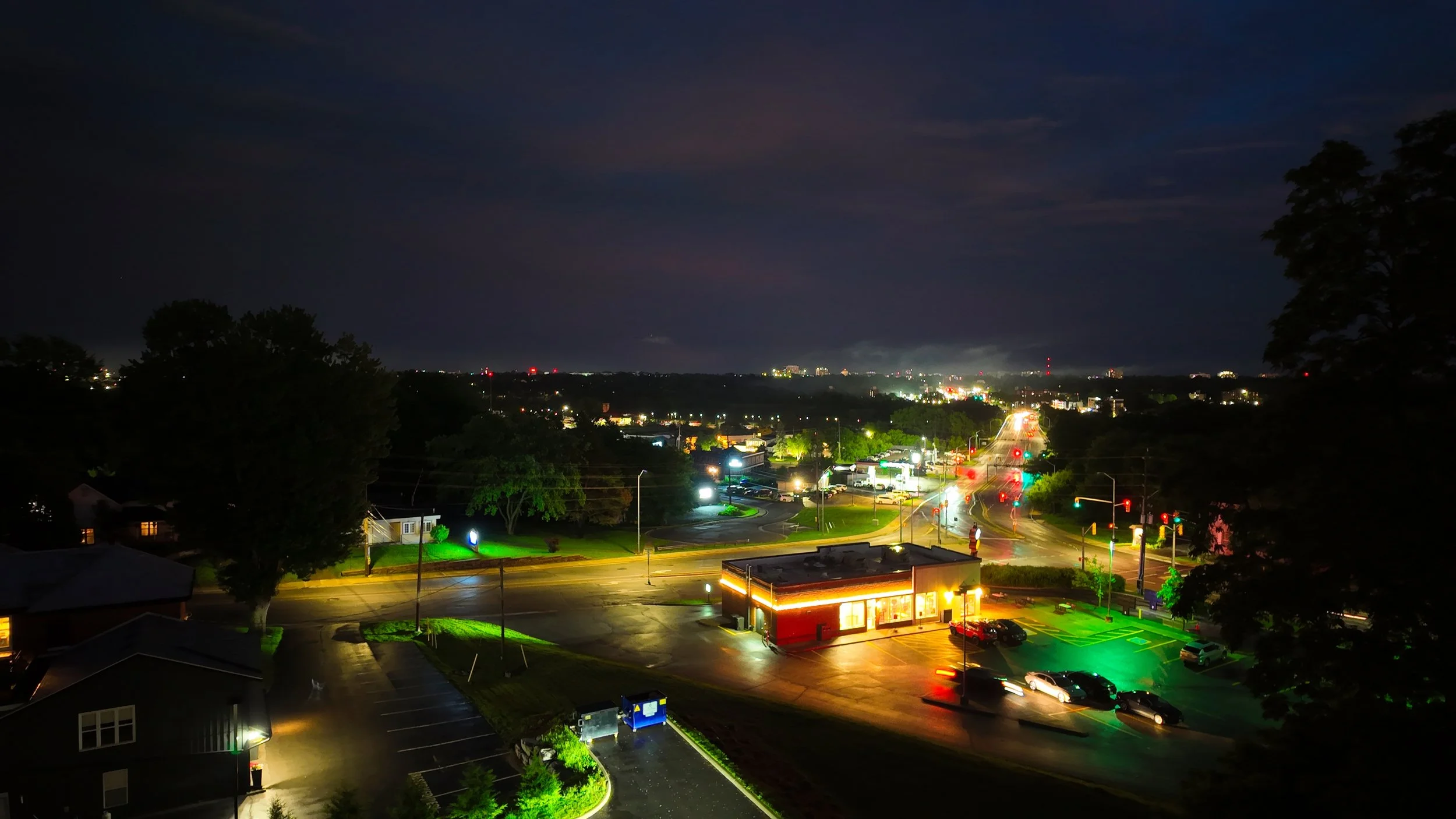 Nighttime cityscape with illuminated streets, buildings, and traffic lights, and a dark sky with some clouds.