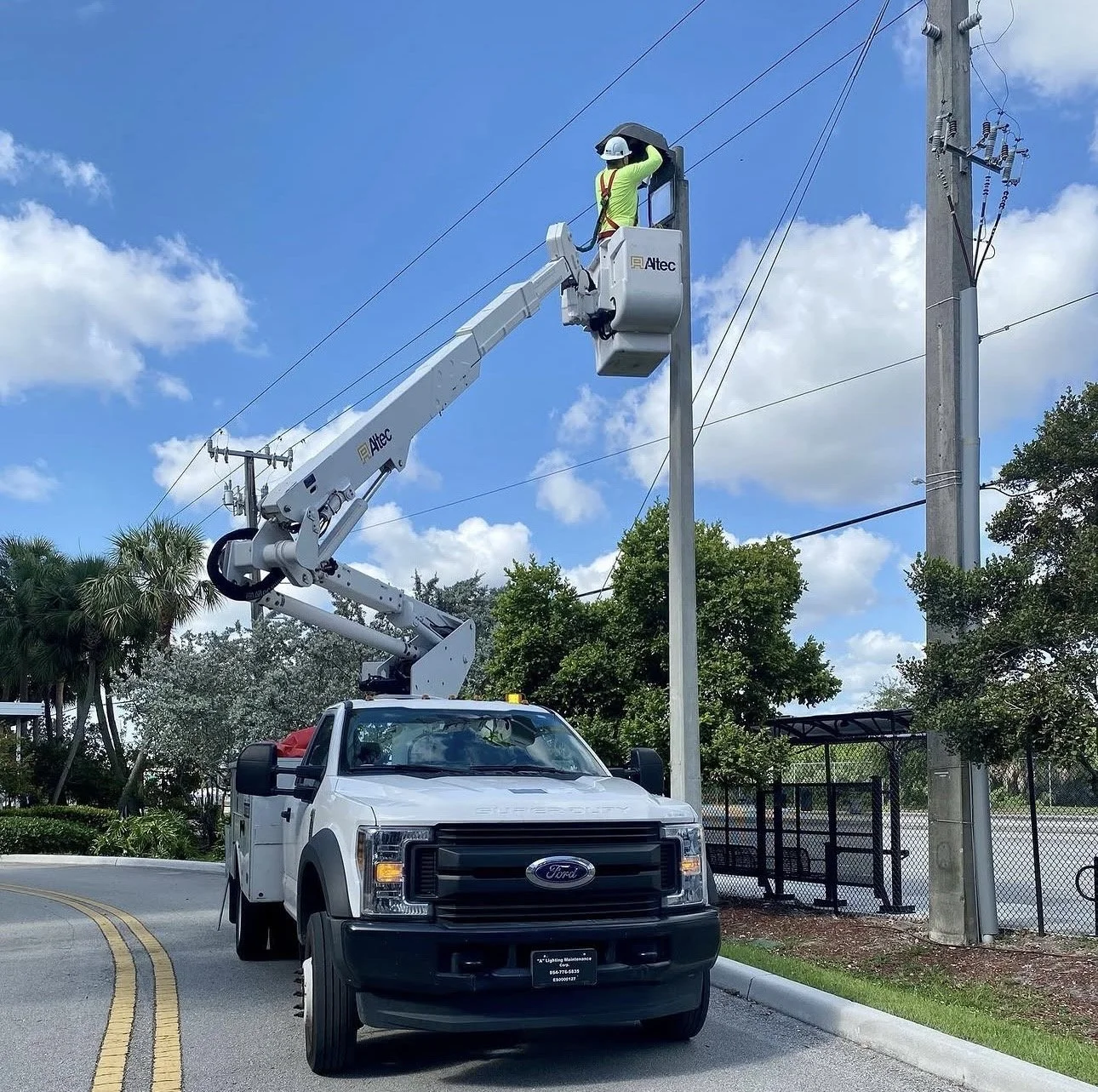 Worker in safety gear repairing a light pole using a bucket lift truck on a sunny day.