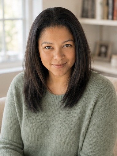 A woman with long dark hair, wearing a green sweater, sitting in a well-lit room with bookshelves in the background.