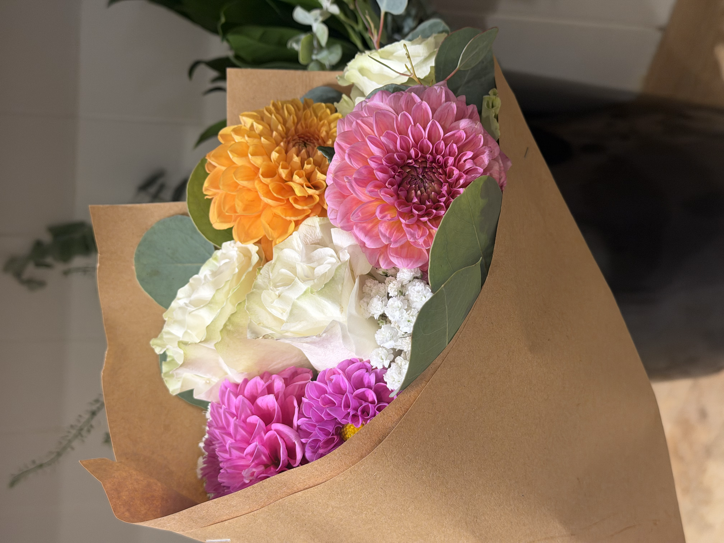 Colorful bouquet of pink, orange, white, and green flowers wrapped in brown paper.