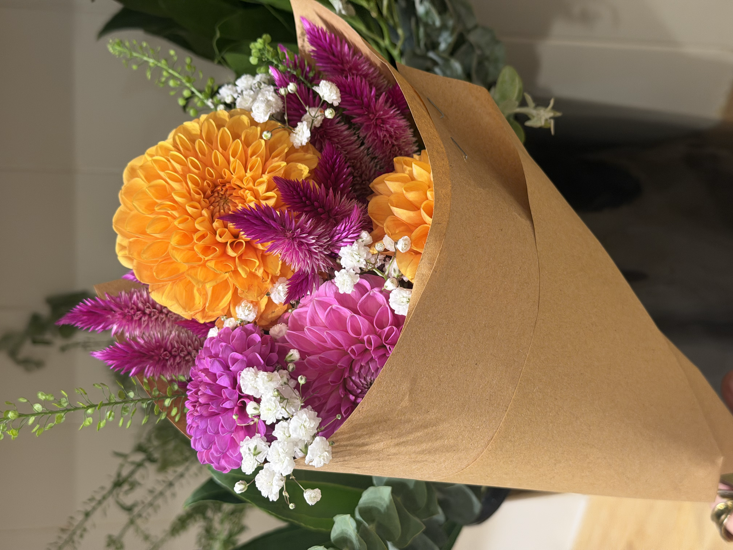 A bouquet of bright orange, pink, purple, and white flowers wrapped in brown paper.