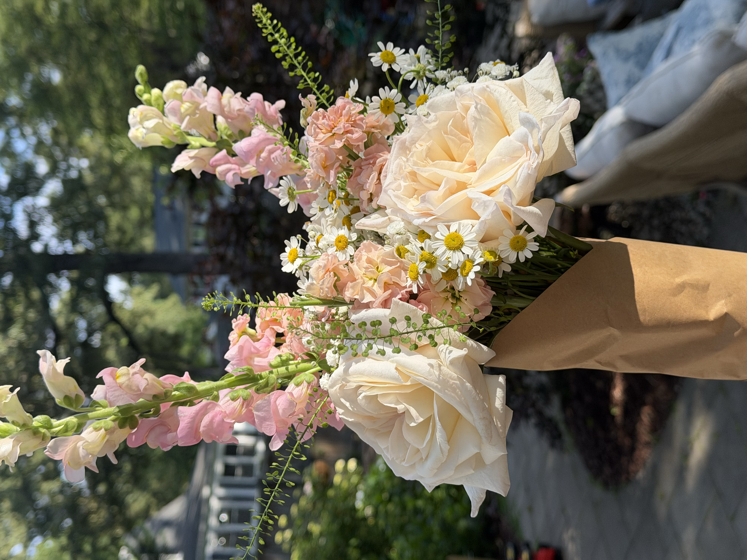 A bouquet of pink, white, and cream flowers with green foliage against a blurred outdoor background.