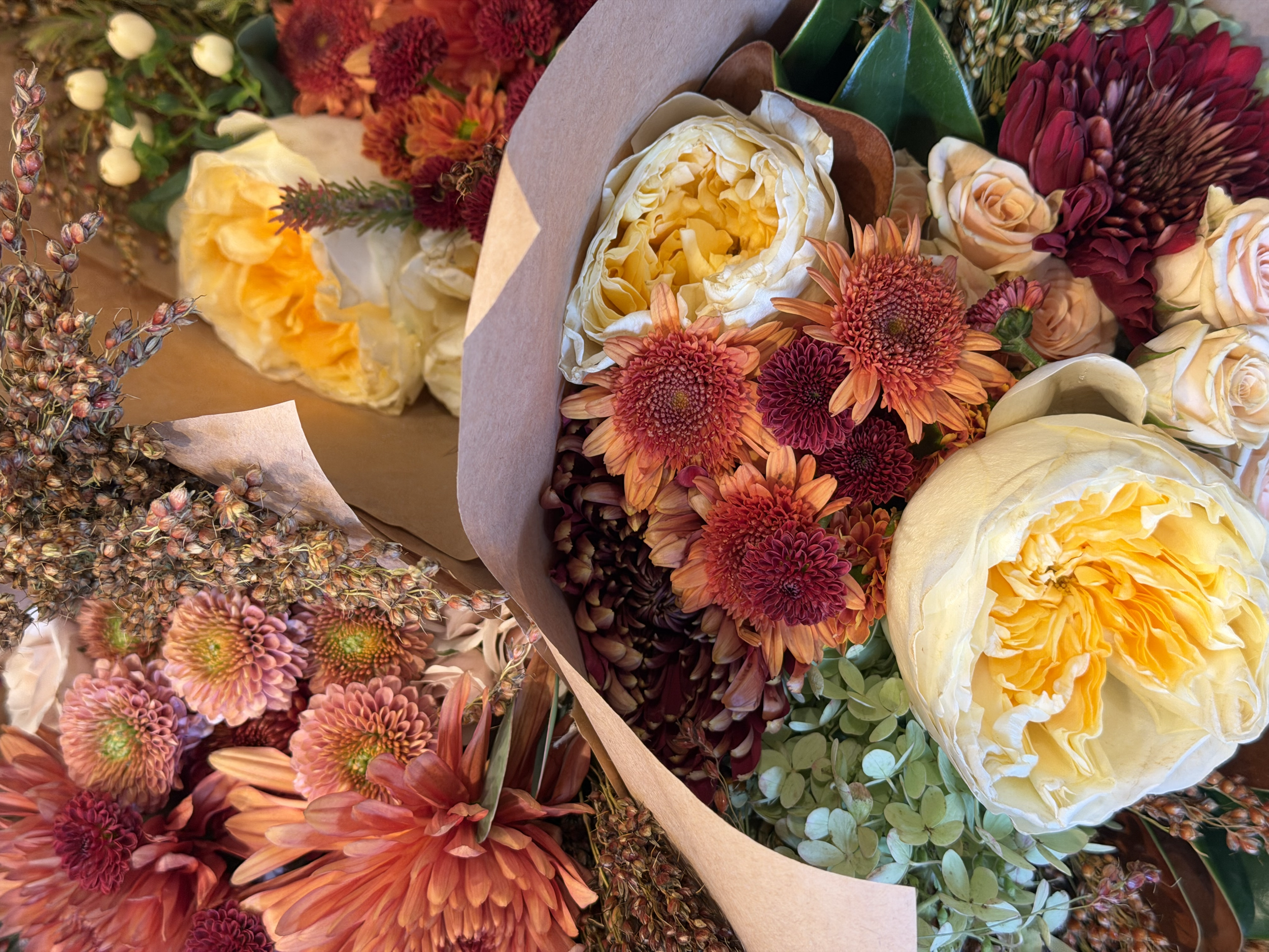 Colorful bouquet of various flowers including large white and yellow peonies, orange and red dahlias, pink chrysanthemums, and greenery.