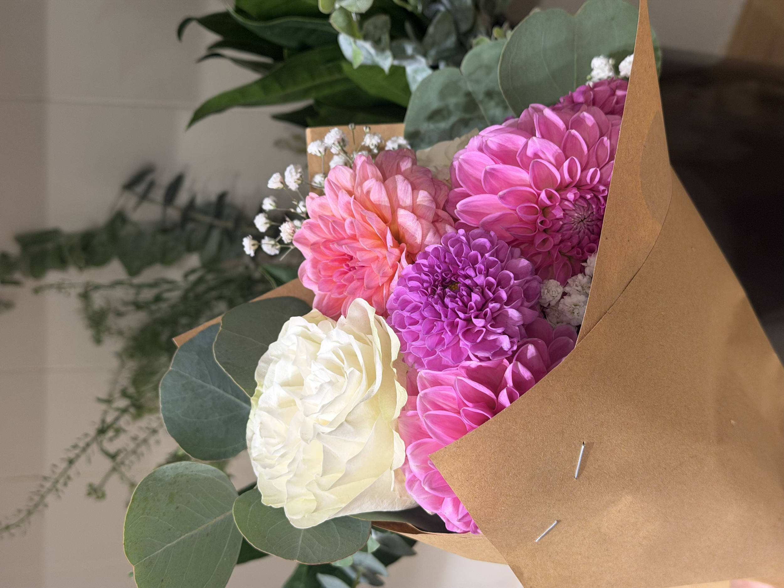 A bouquet of pink, purple, white, and cream-colored flowers wrapped in brown craft paper.