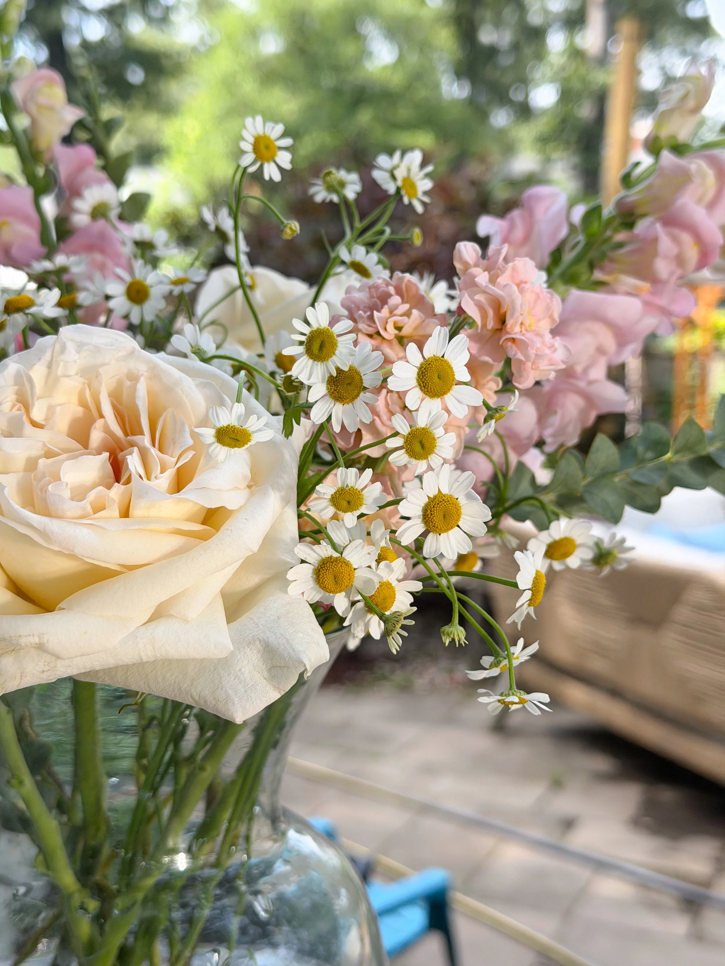 Close-up of a bouquet with white roses, pink stock flowers, and daisies in a clear glass vase.
