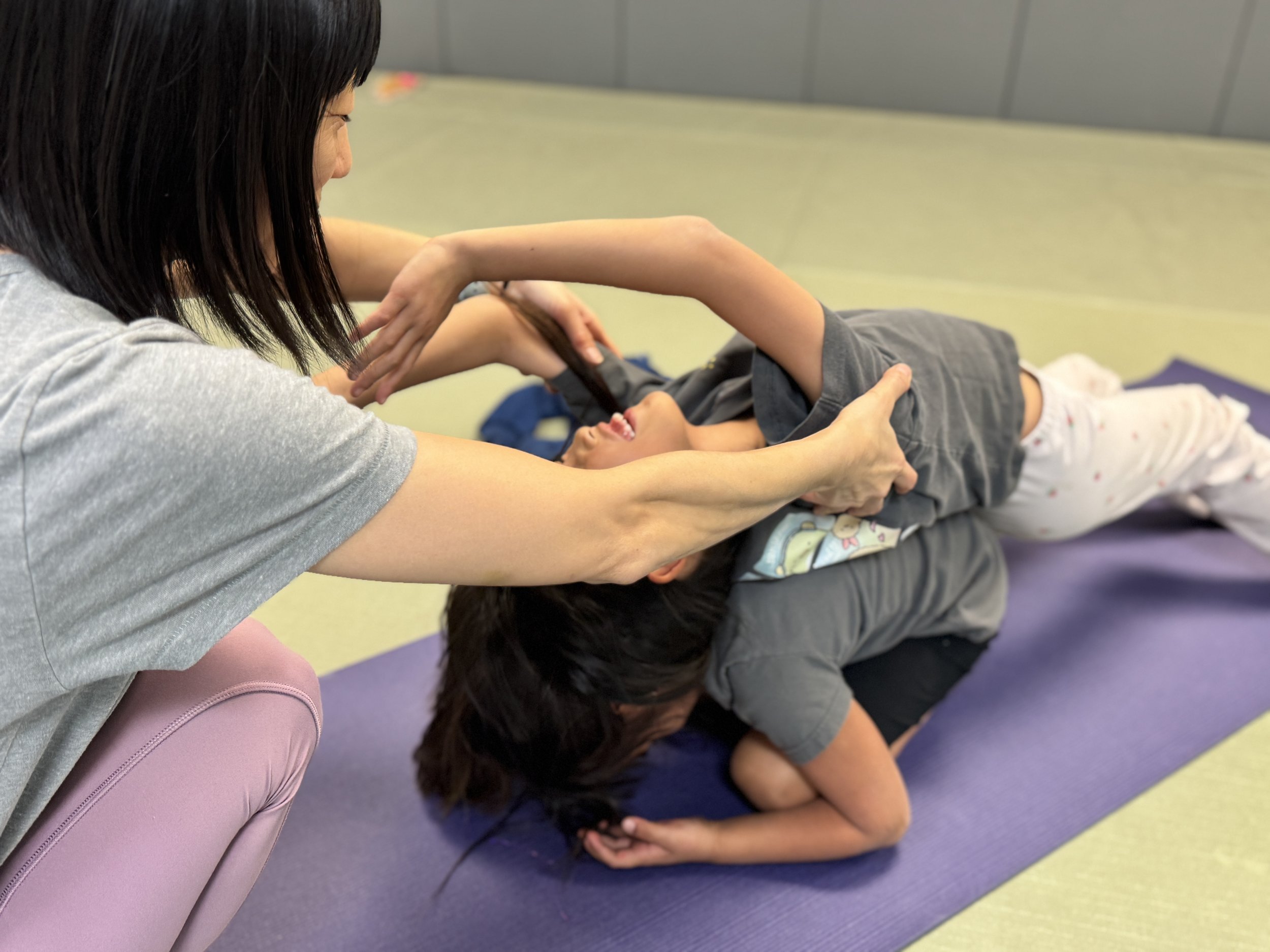 A woman helping a child with a stretch or yoga pose on a colorful yoga mat.