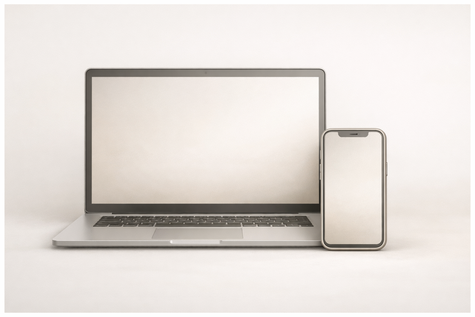 A silver laptop computer with a blank screen and a smartphone with a blank screen, placed on a white surface against a light background.