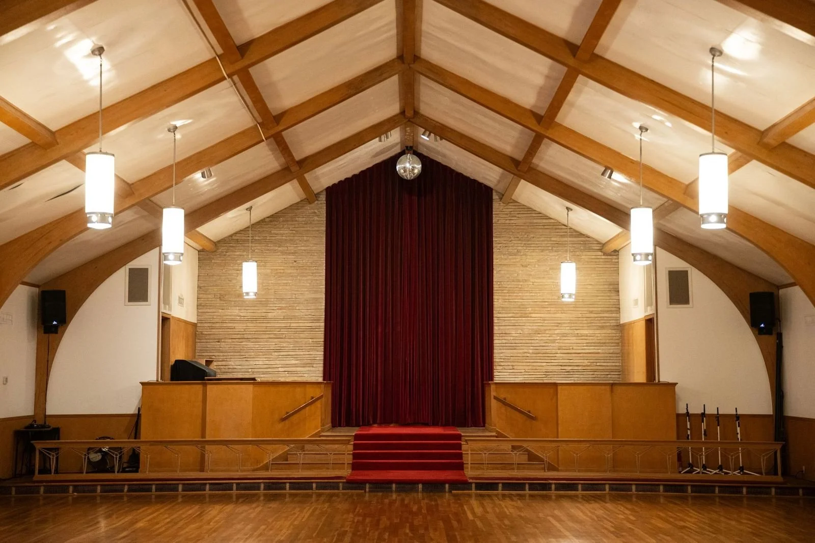 Empty stage with red curtain in a wooden auditorium with hanging pendant lights.