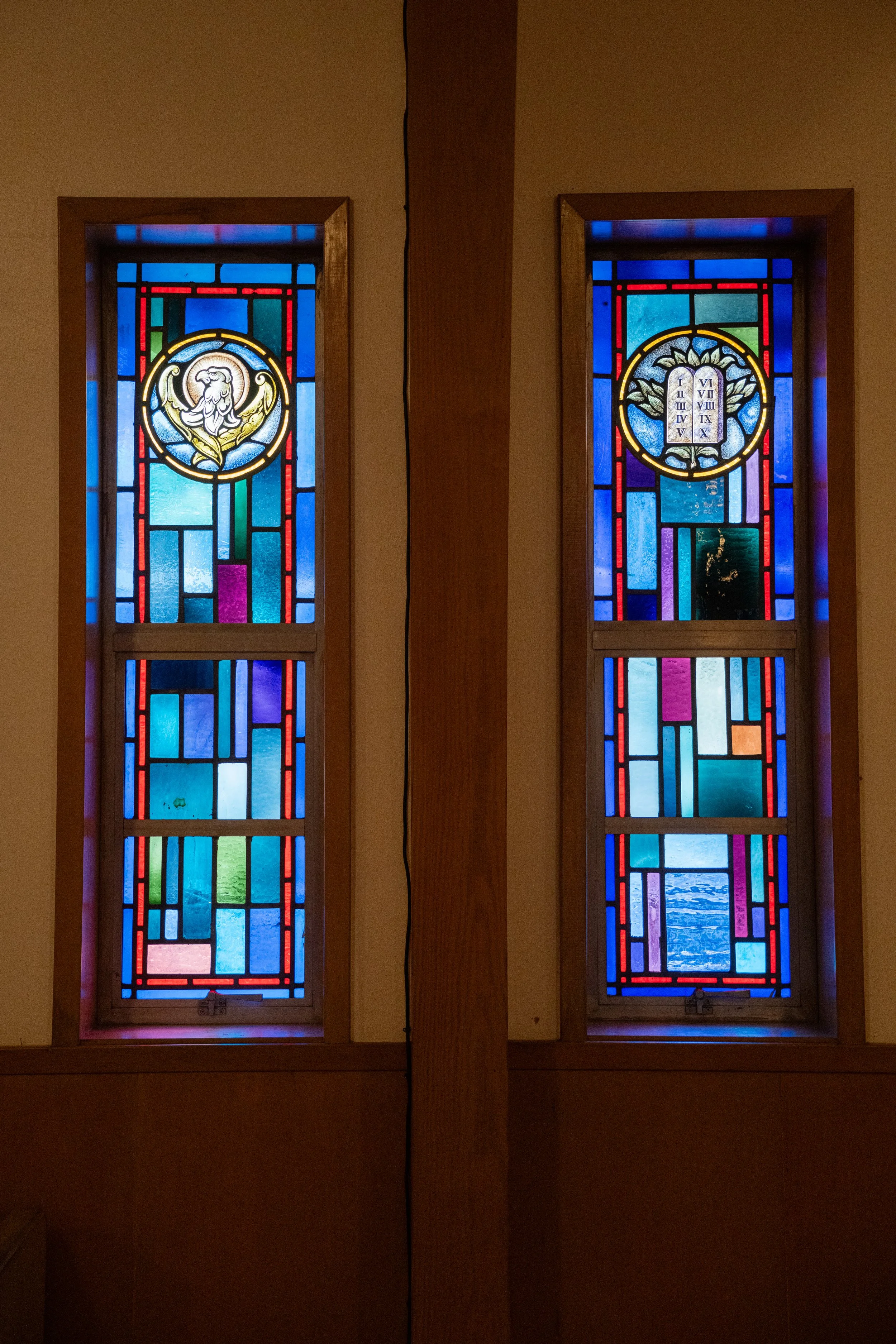 Two stained glass windows with different designs, surrounded by wooden frames, and separated by a wooden vertical beam.