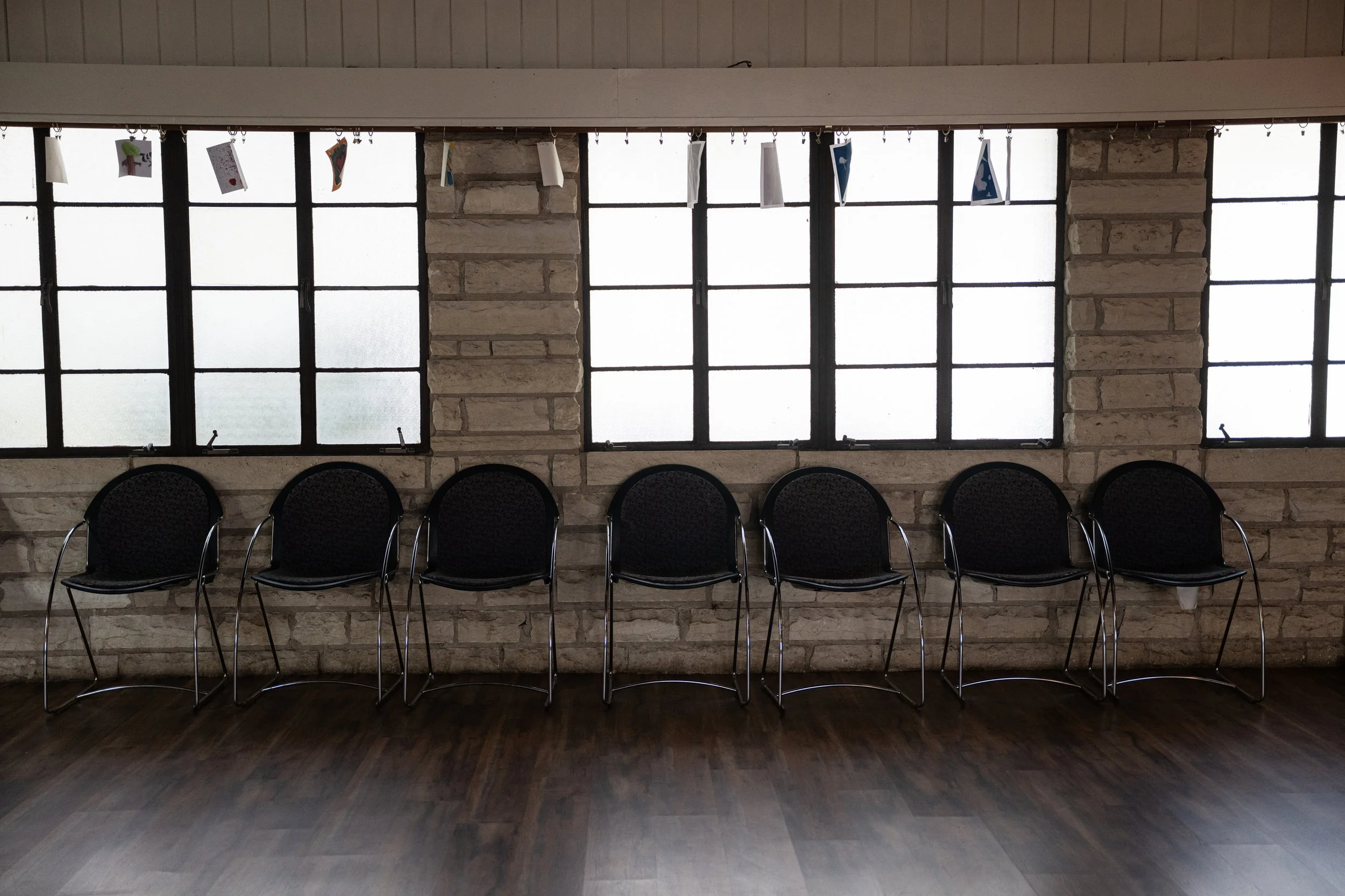 Empty chairs in front of large frosted windows with hanging artwork above.