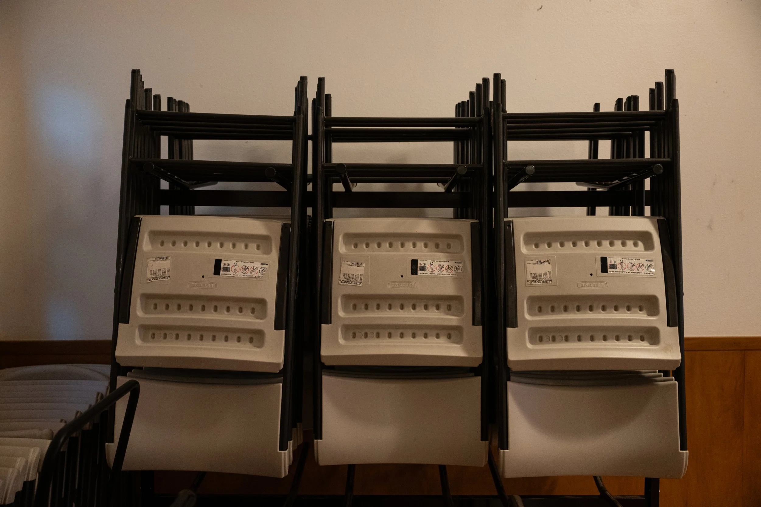 Stacked beige plastic chairs with black metal frames leaning against a plain beige wall.