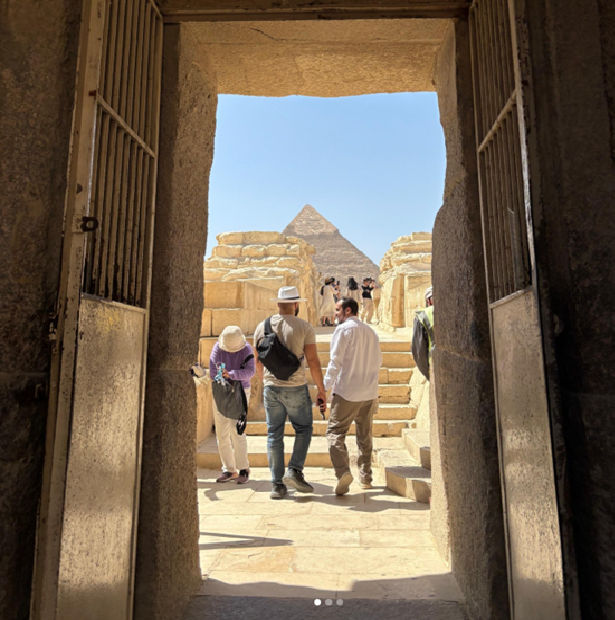 Tourists exploring the Great Pyramid of Giza from an ancient stone entrance, with pyramids visible in the background under a clear sky.