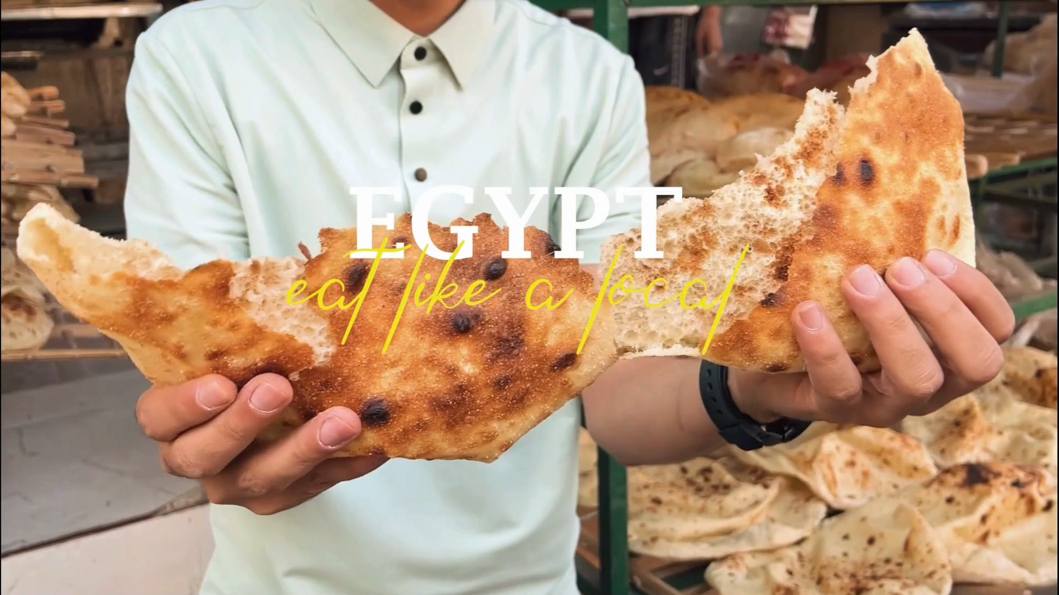 Person holding large piece of Egyptian bread in a bakery with bread loaves in the background.