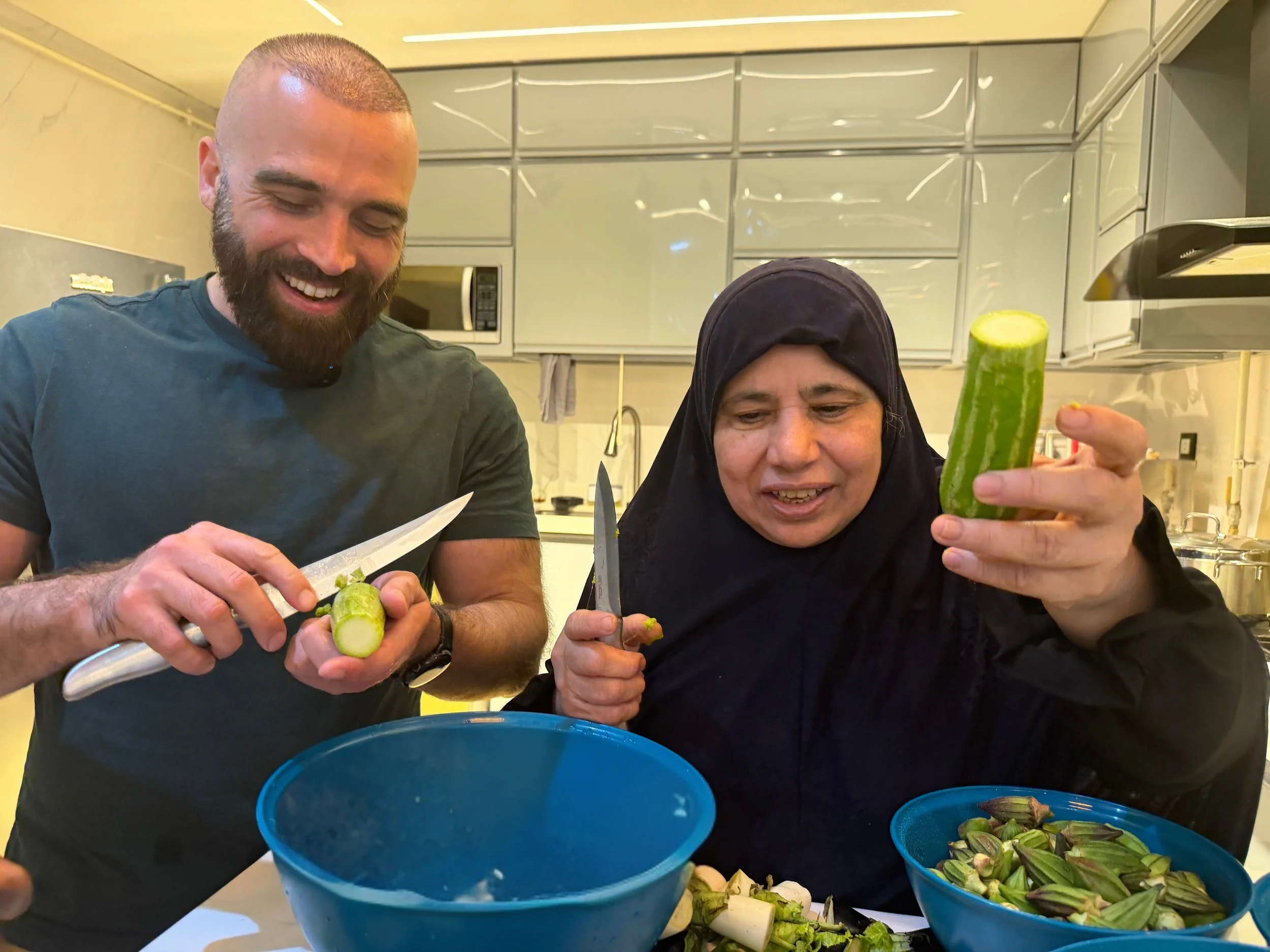 Two people preparing vegetables in a kitchen, with a man and a woman smiling as they work, surrounded by bowls of chopped vegetables.
