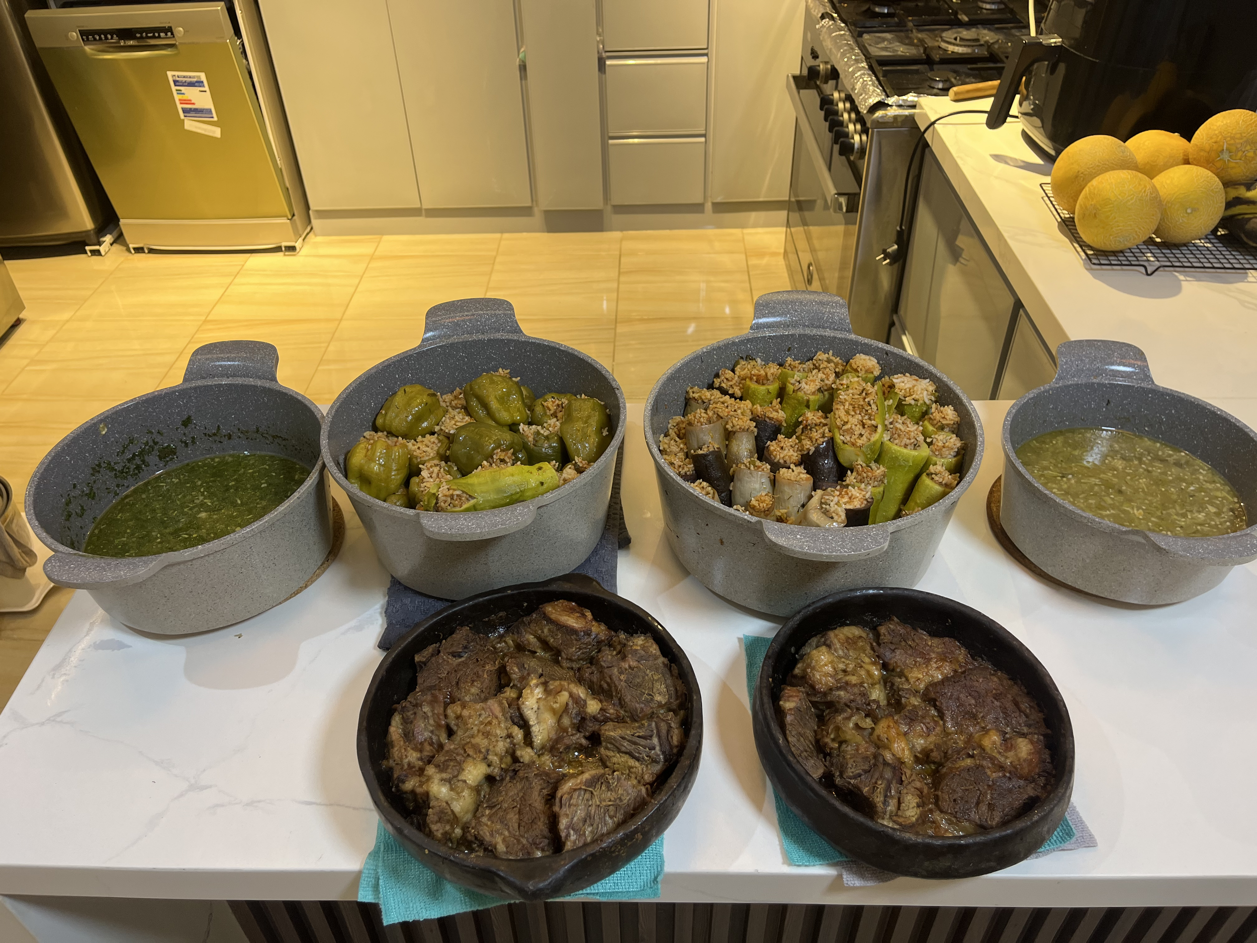 Several pots of cooked stuffed peppers and other dishes on a white counter in a kitchen.