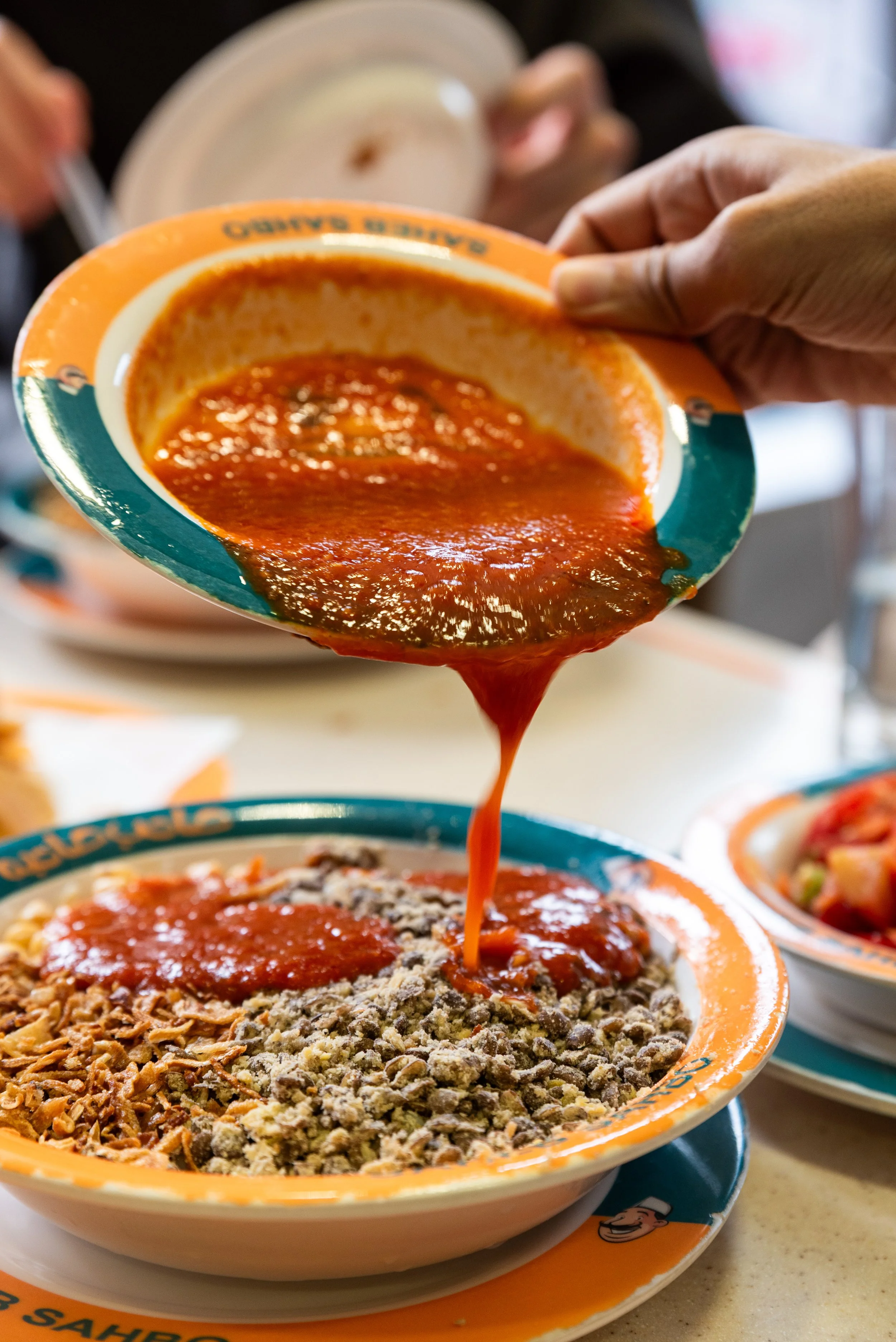 A bowl of spaghetti with red marinara sauce being poured over it, surrounded by other dishes, in a restaurant setting.