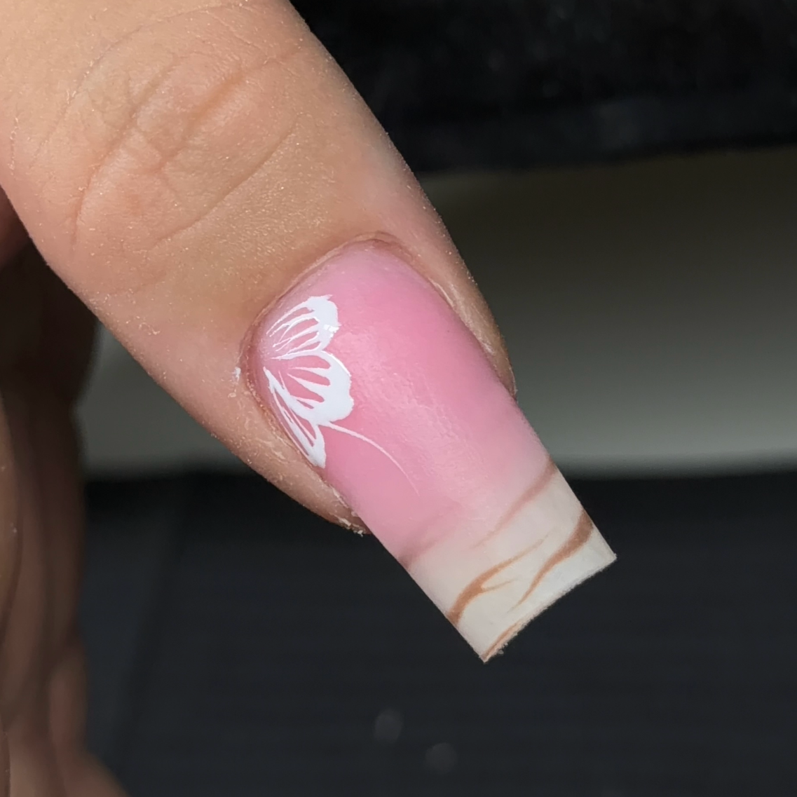 Close-up of a person’s thumbnail with a pink base coat, white butterfly nail art, and a clear tip design.