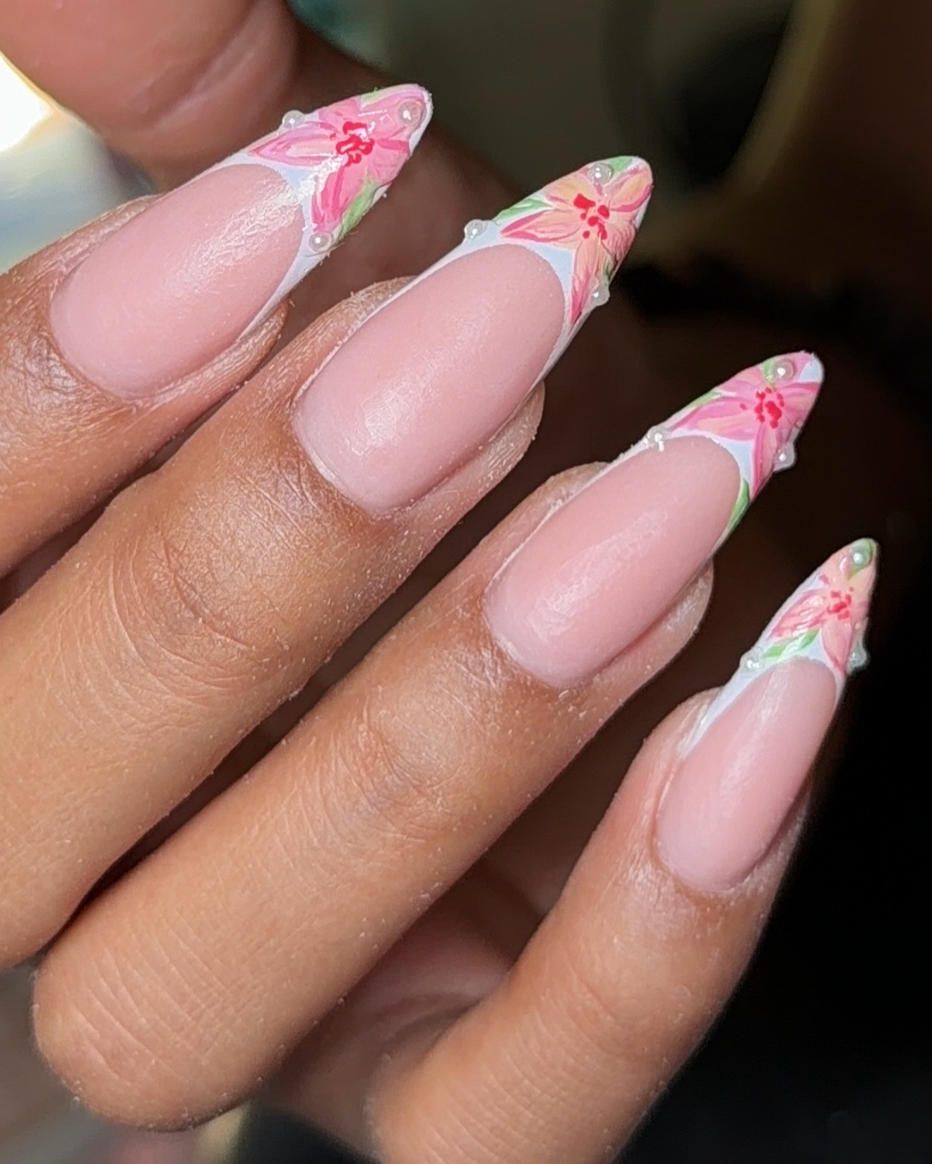 Close-up of a person's hand with long, almond-shaped nails decorated with pink floral nail art and small white pearls.