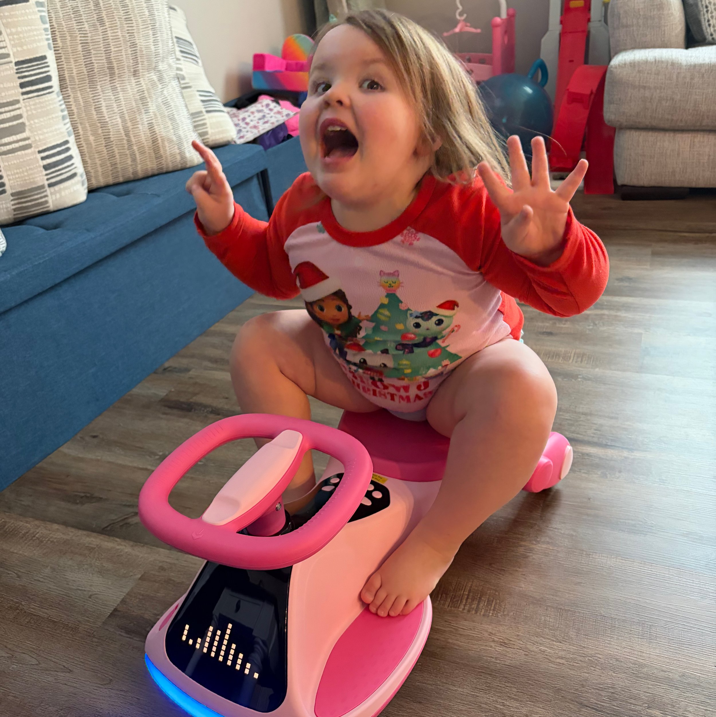 Bella Grace smiling while sitting on her pink motorbike and holding up four fingers to celebrate turning four years old, reflecting her joyful spirit, confidence, and excitement for life.