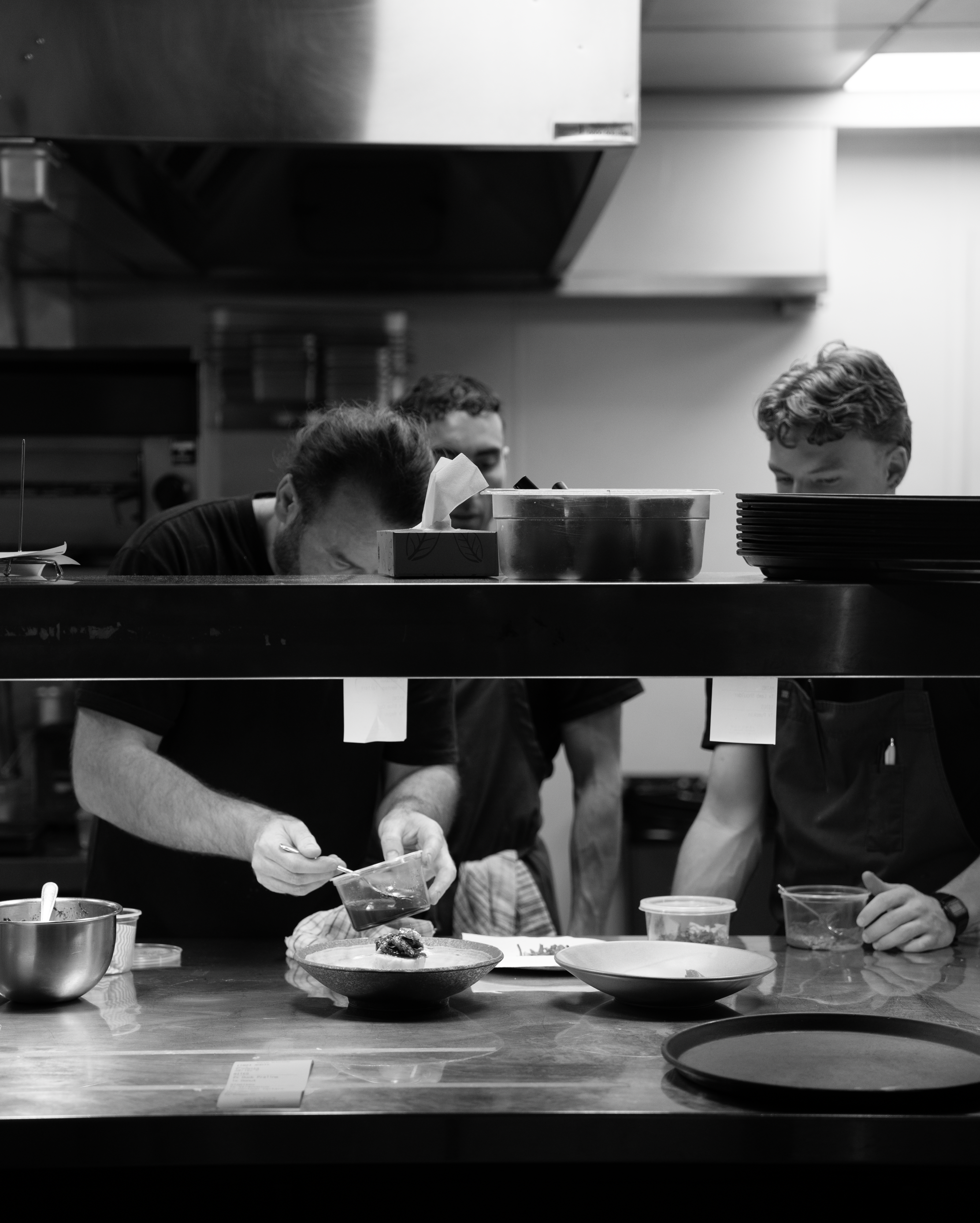 People working in a commercial kitchen preparing food, with bowls, plates, and ingredients on the counter.