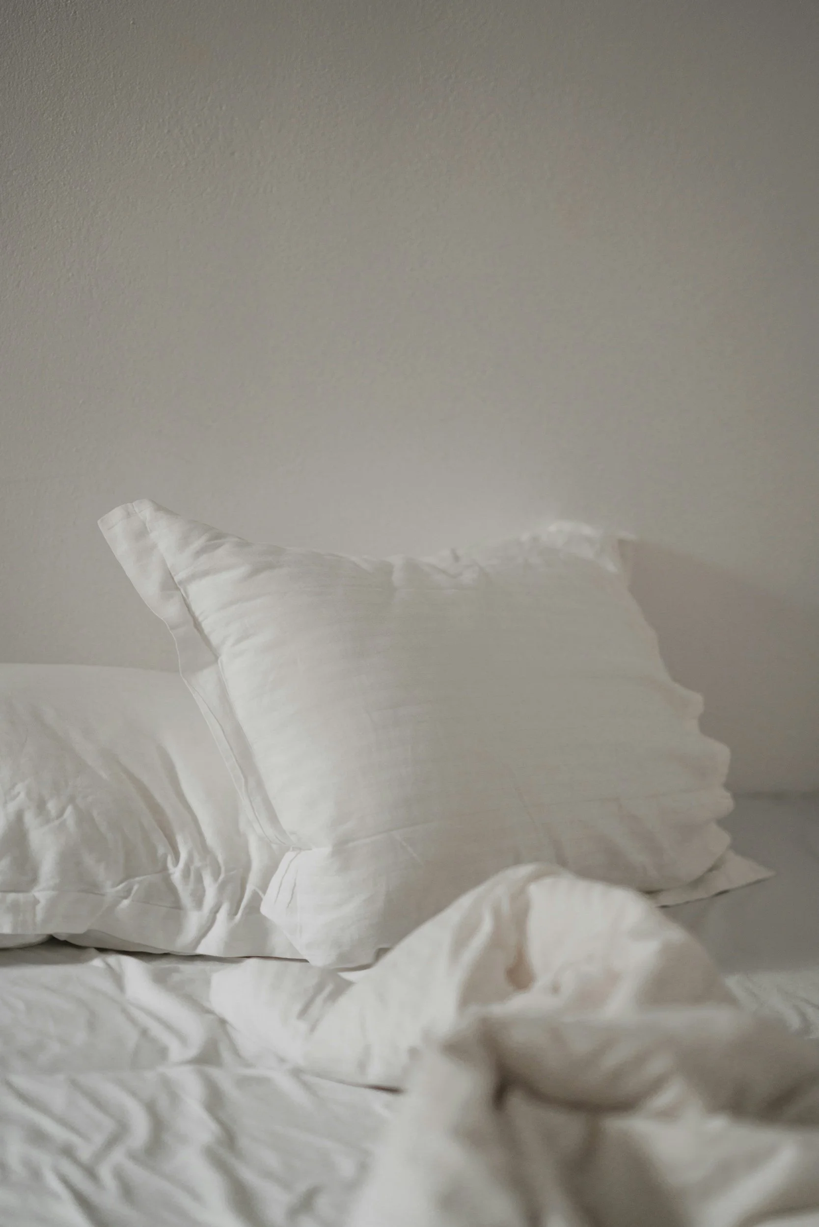 A crumpled white pillow on a bed with a plain light-colored wall in the background.