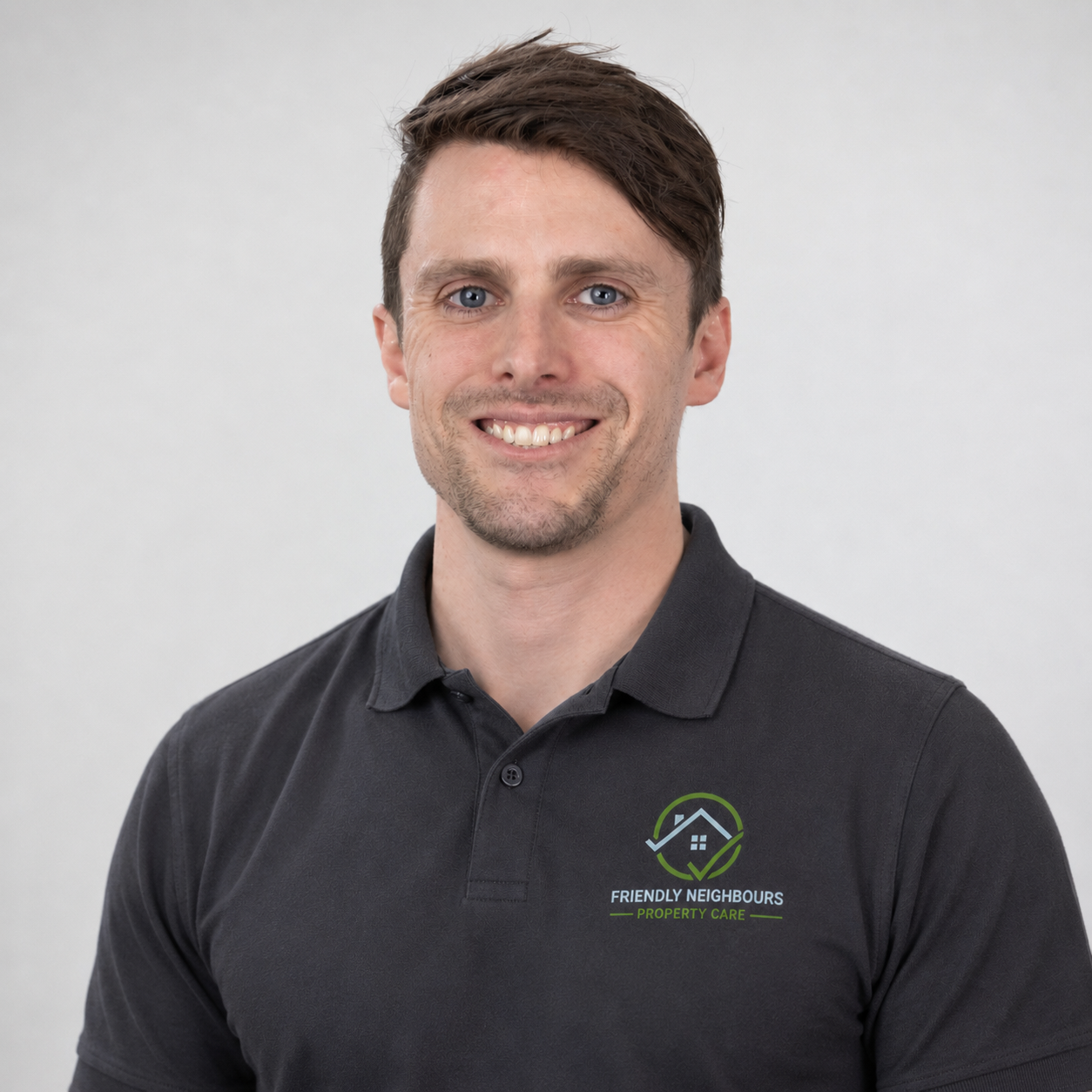 A man with short brown hair smiling, wearing a black polo shirt with a logo for Friendly Neighbours Property Care, standing against a plain light gray background.