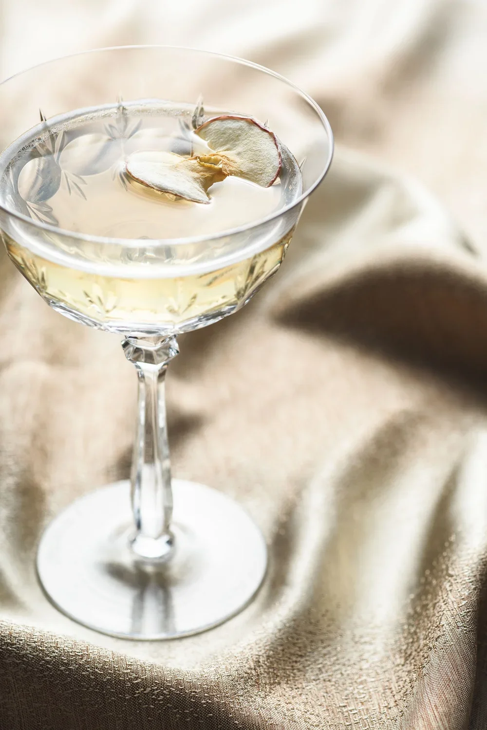 Commercial beverage photo of a champagne coupe with floating apple slice by photographer Amy Carson.