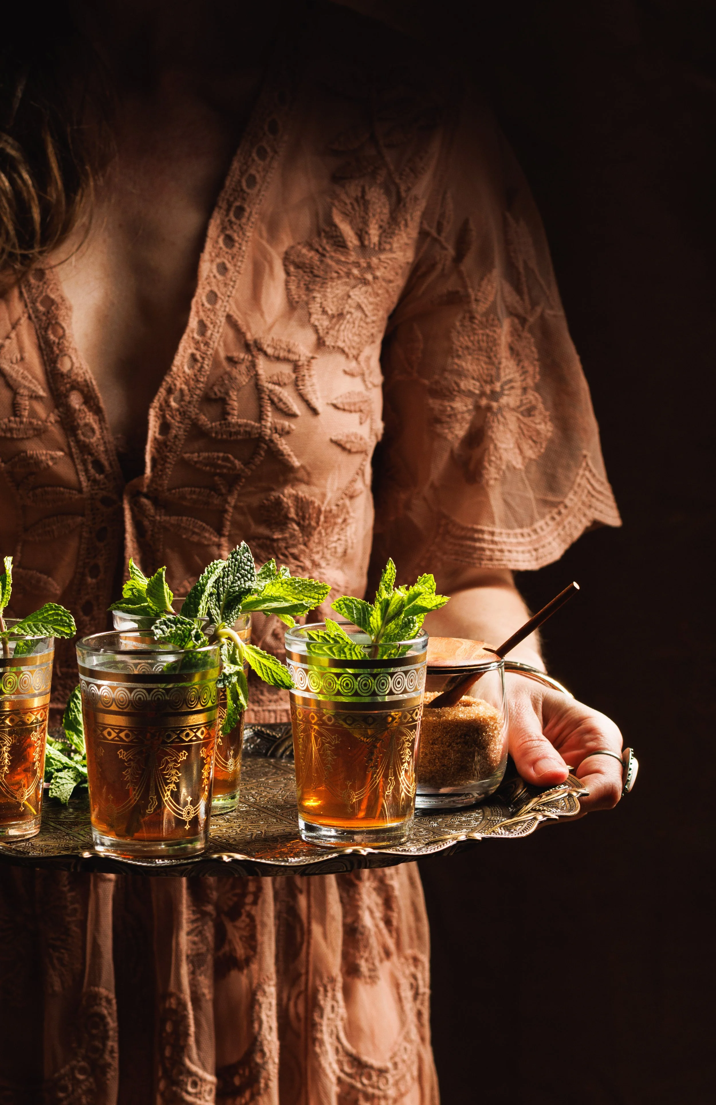 Moody commercial beverage photo of a woman wearing a bohemian dress holding a tray of mint tea.