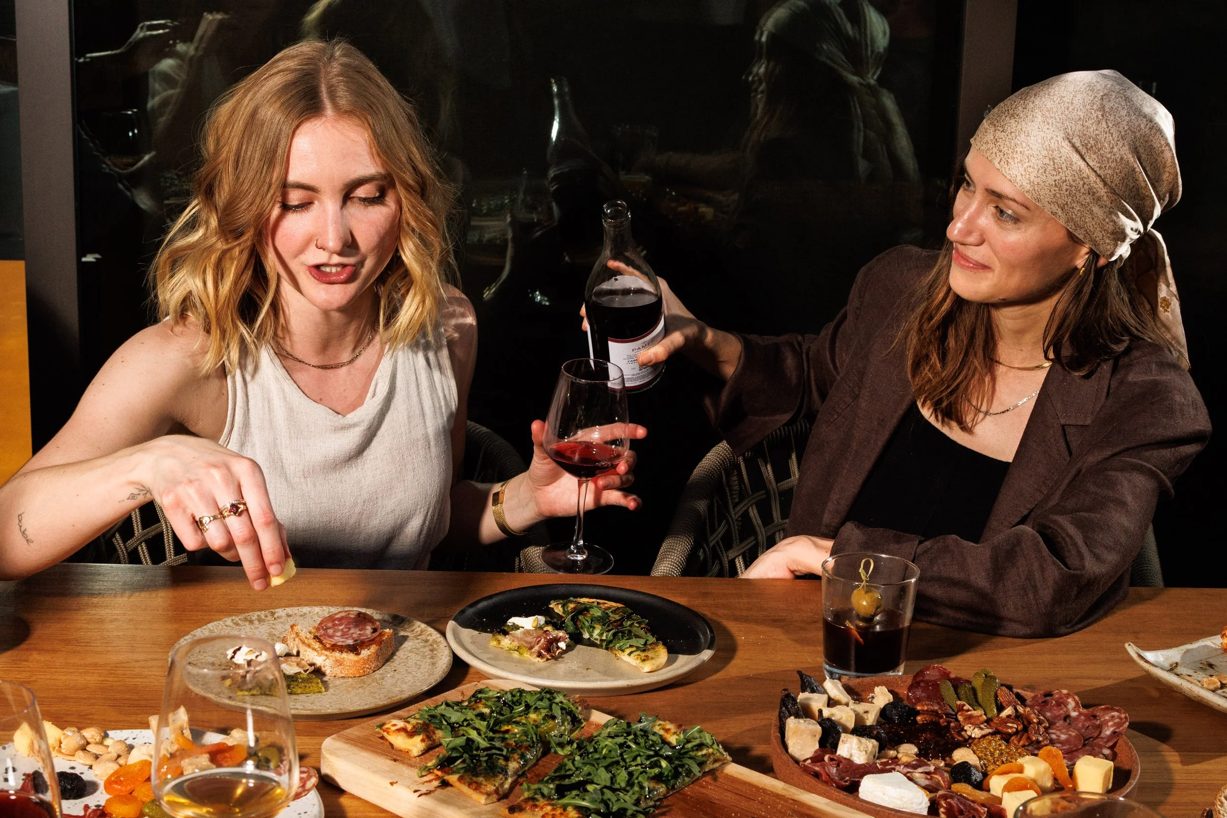 Commercial lifestyle photo of two women eating and drinking wine for a hospitality campaign.