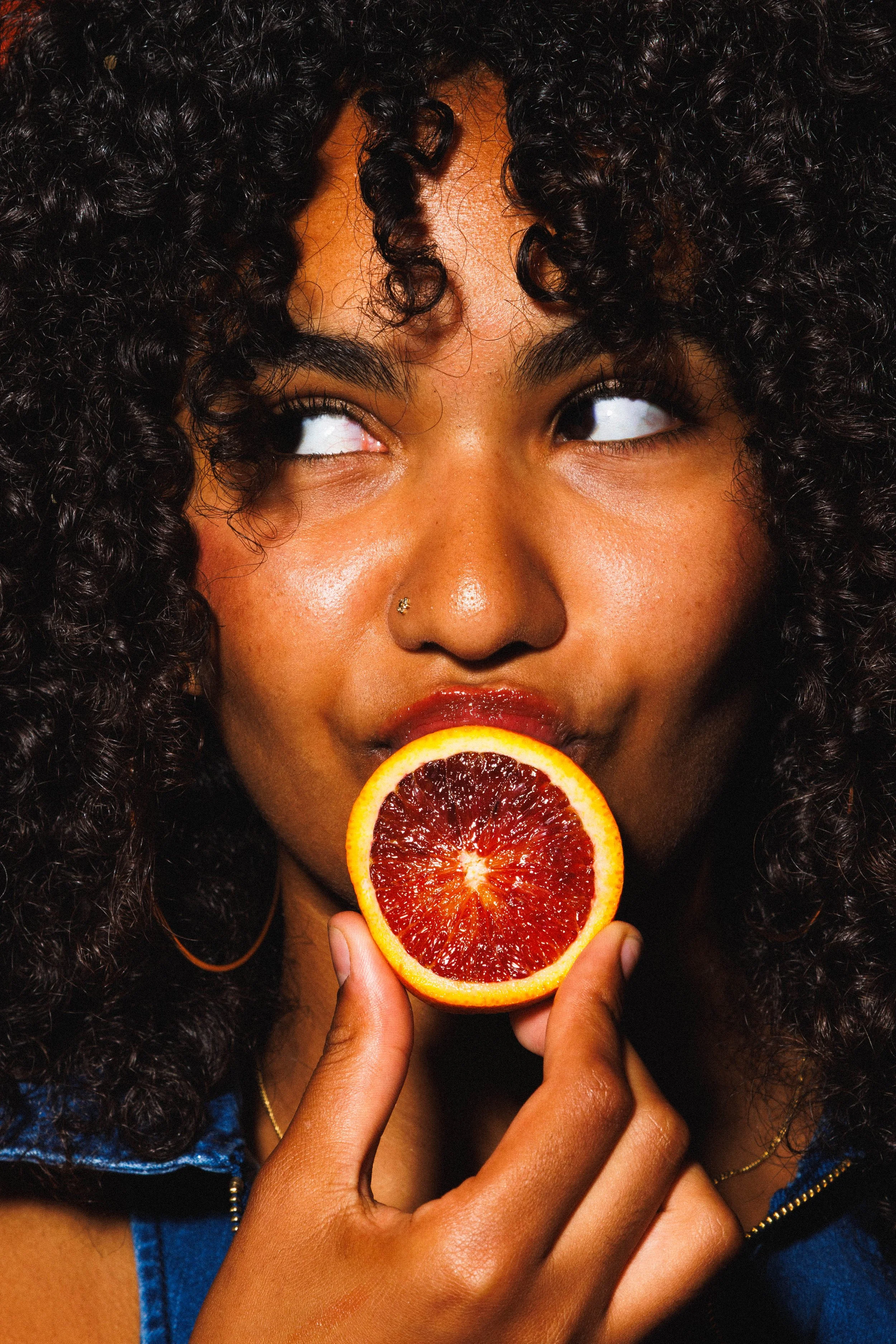 Commercial lifestyle portrait of a young women with an orange slice on her lips for an advertisement.