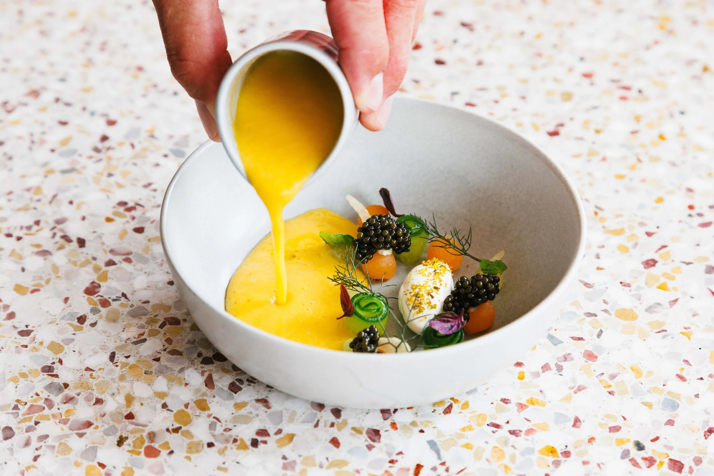 Editorial food photo of a chef plating an elegant dish.