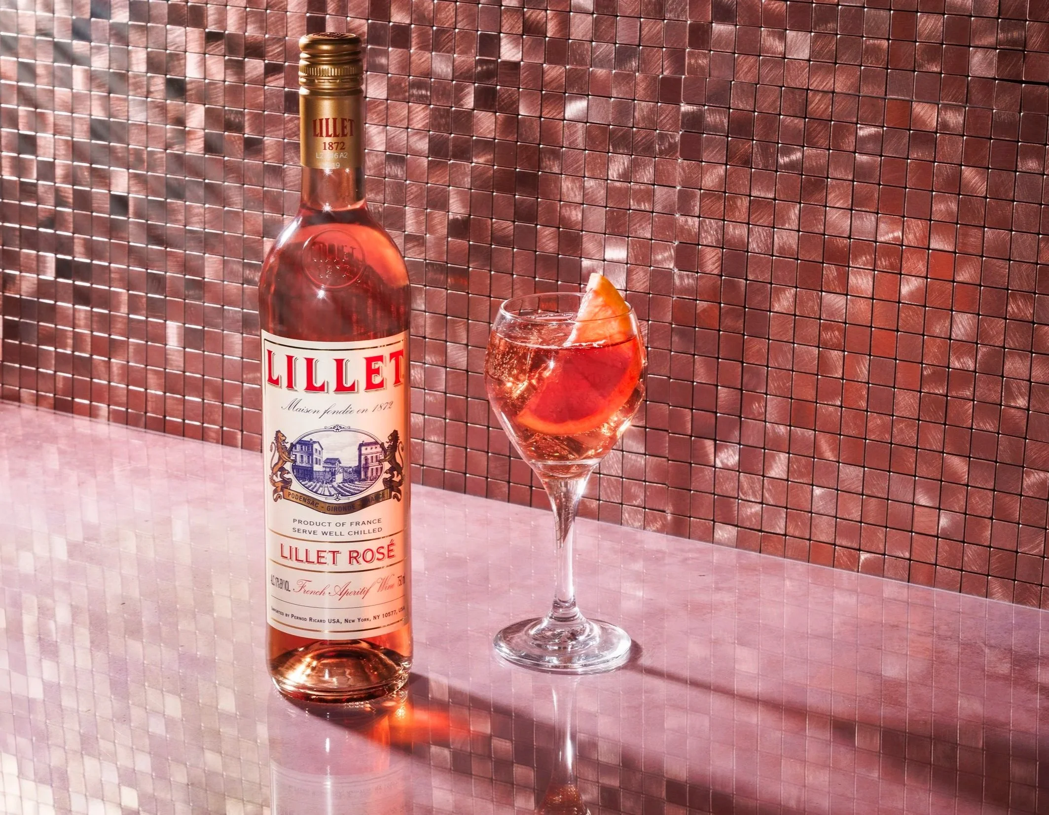 Commercial beverage product photo of a Lillet rose wine bottle and glass in a glam, sparkly style.