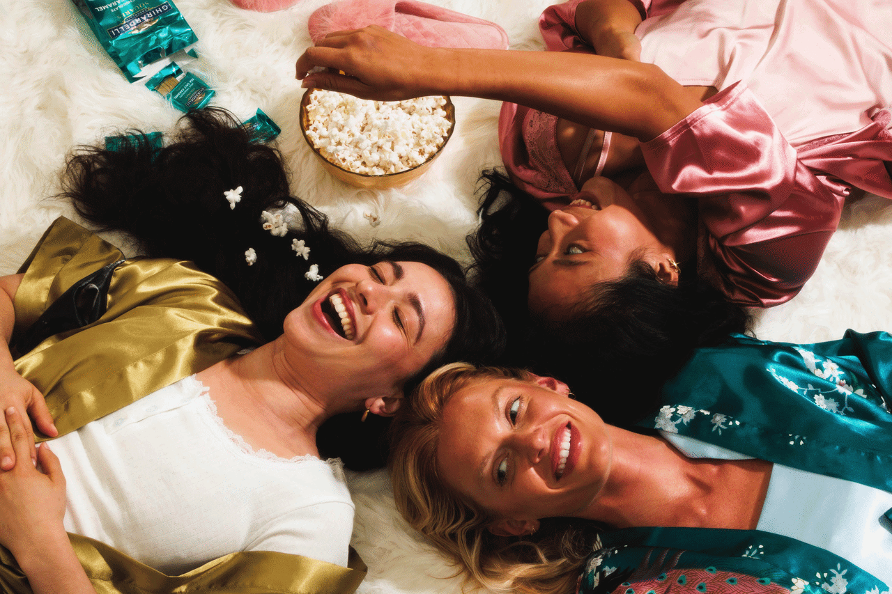 Commercial lifestyle gif of three women eating popcorn and laughing.