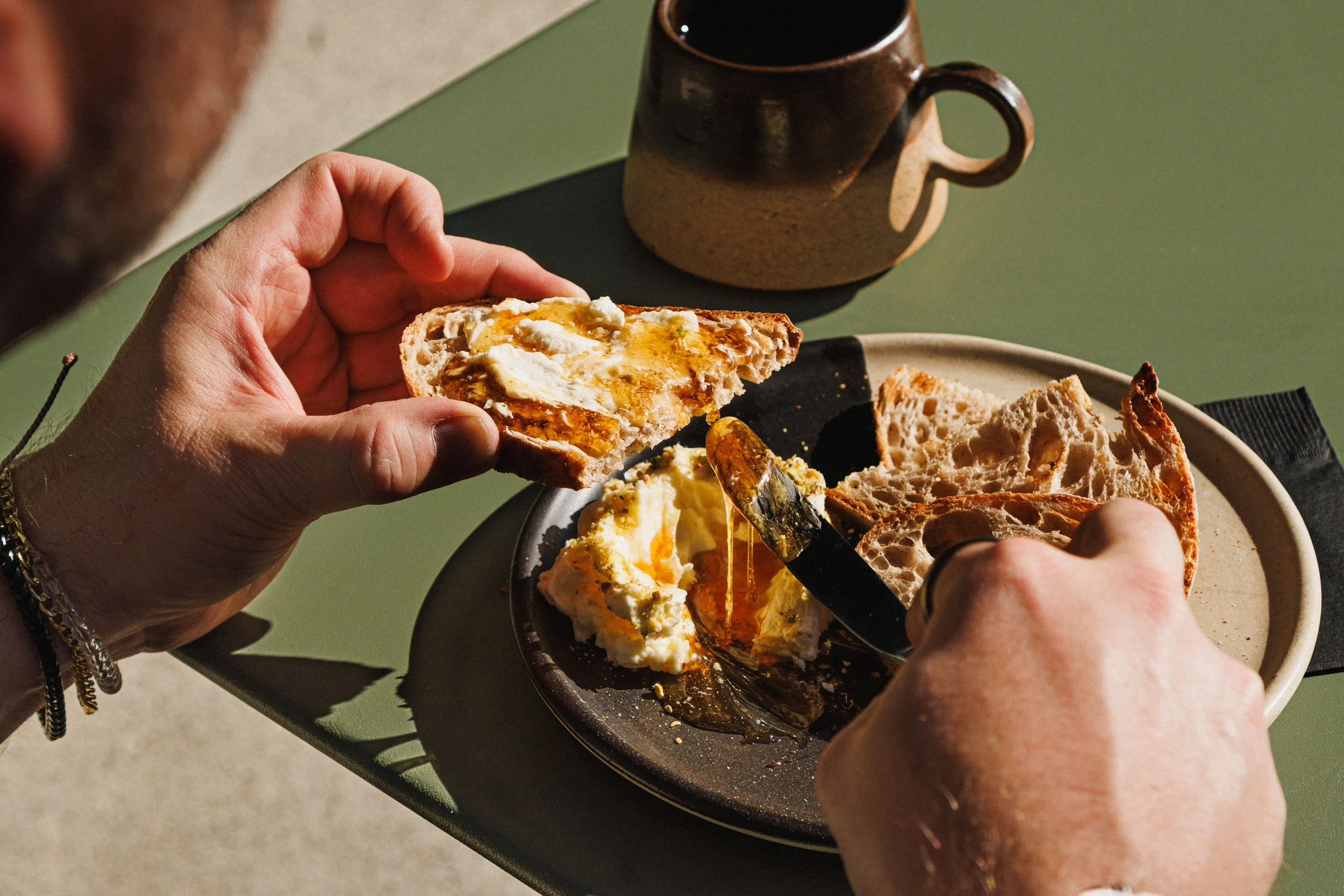 Commercial food photo of a man spreading honey on bread at Heavenly Bodega, in San Diego.