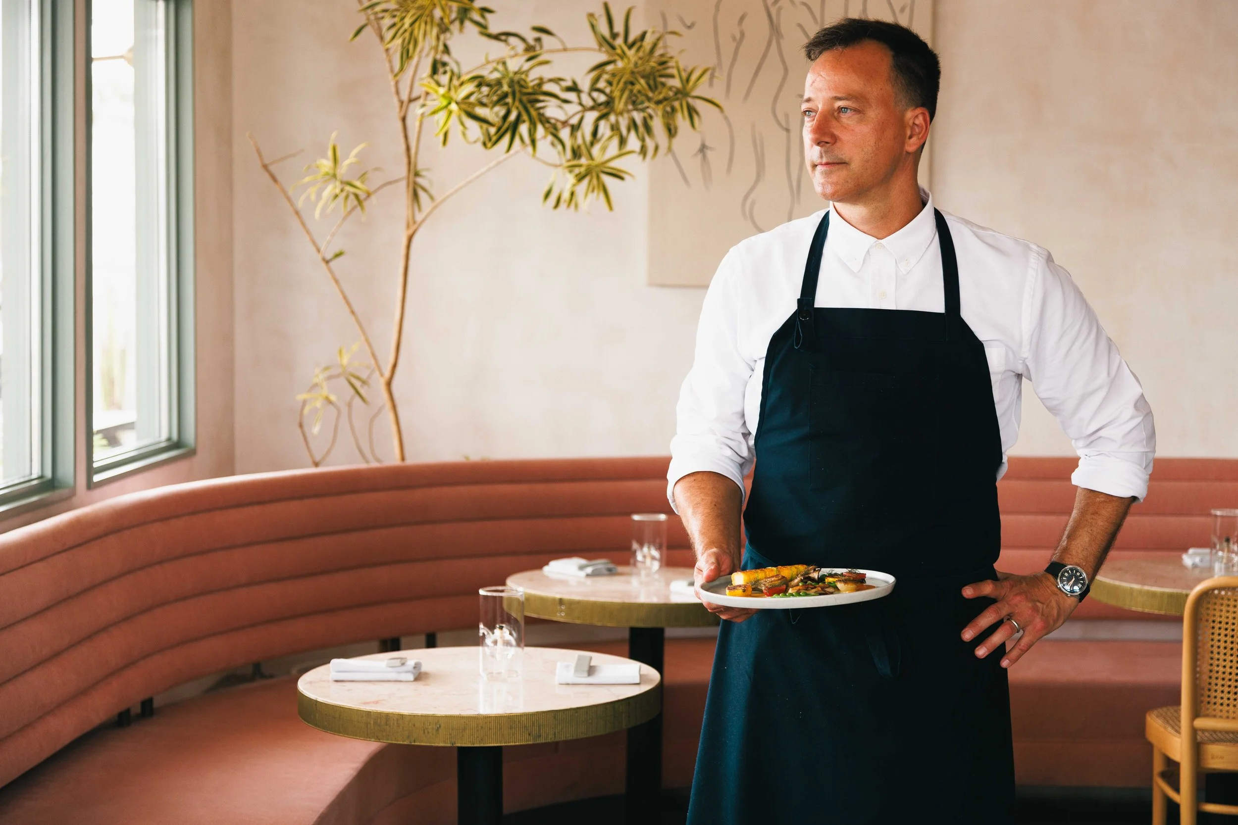 Hospitality portrait of a Michelin starred chef holding a plate of food in his restaurant.